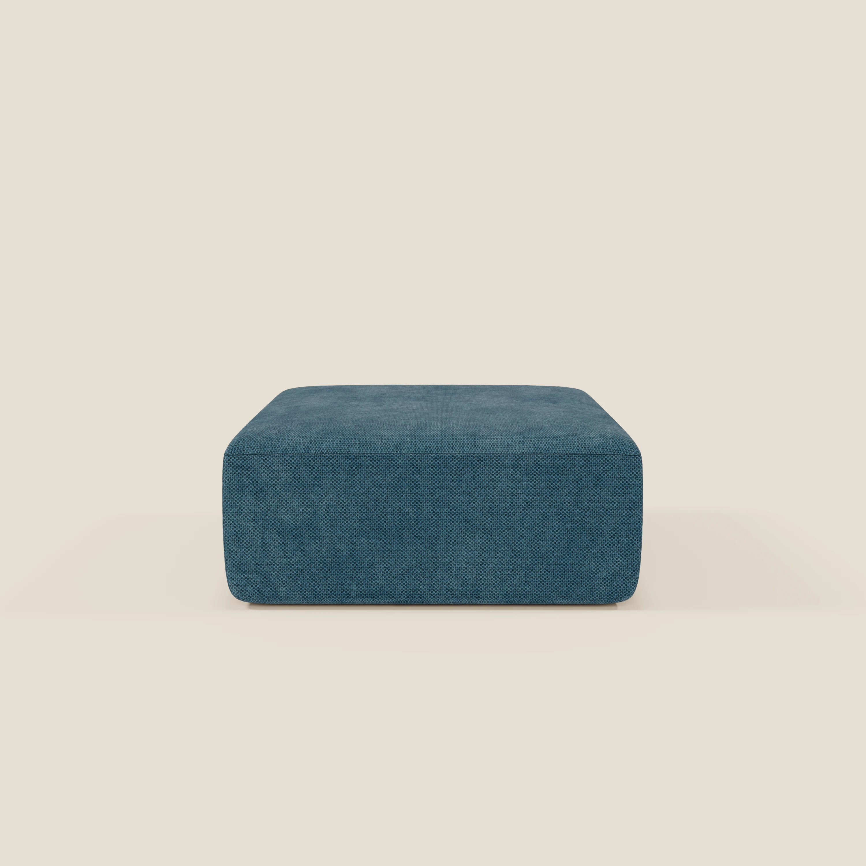 Il pouf modulo Grande Fratello edition petrolio di BonBon di Divani.Store, un pouf quadrato e basso di colore blu dal design minimalista e dalla morbida imbottitura, si staglia su uno sfondo beige chiaro, ideale per un'elegante configurazione di divano modulare.