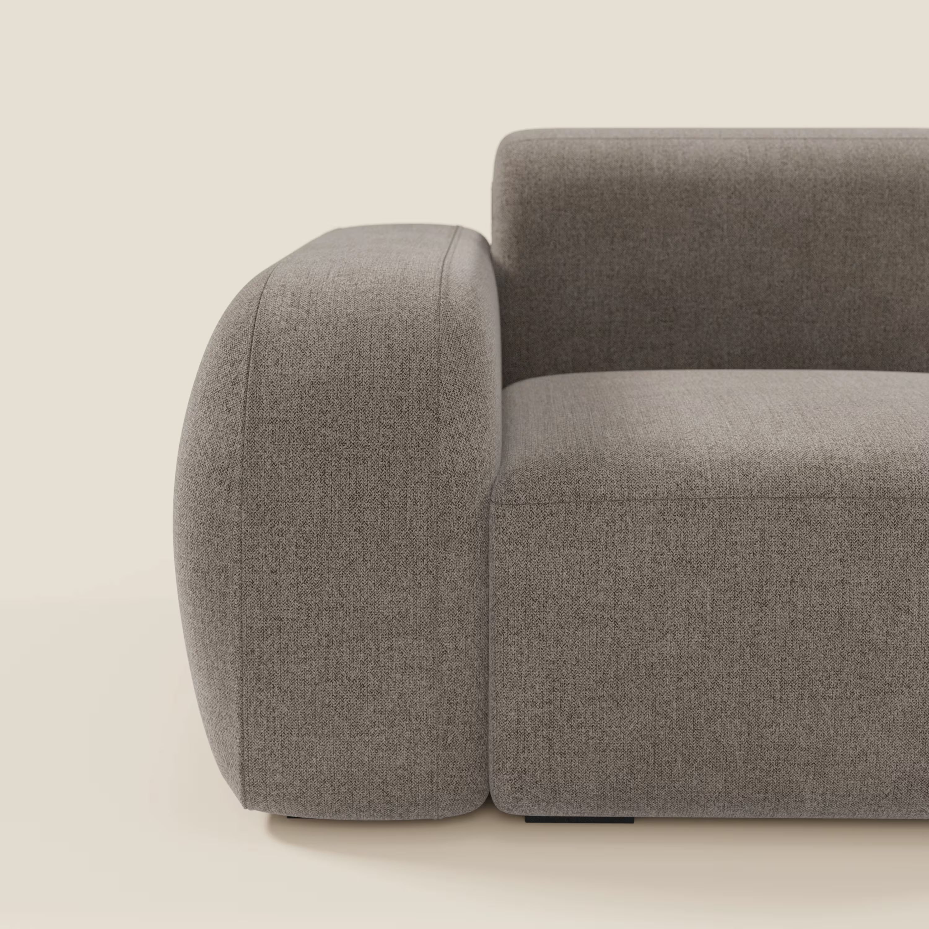 Un primo piano del modulo BonBon terminale 105 cm sinistro o destro di Divani.Store, caratterizzato da braccioli spessi e arrotondati e da uno schienale in tessuto smacchiabile T23 talpa, mette in evidenza il suo design minimalista su uno sfondo beige chiaro.