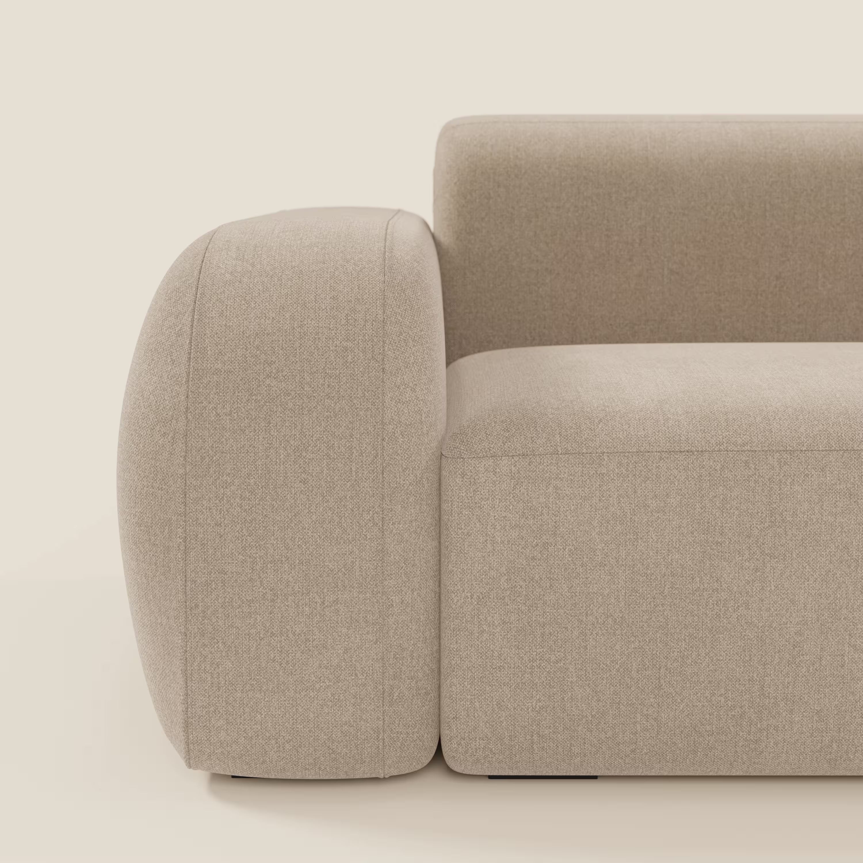 Un primo piano del BonBon Divano modulare Lineare 220 di Divani.Store mostra il bracciolo spesso e arrotondato e la forma squadrata. La seduta unica, in tessuto smacchiabile beige T23, si staglia su uno sfondo semplice color crema chiaro, con un solo bracciolo visibile.