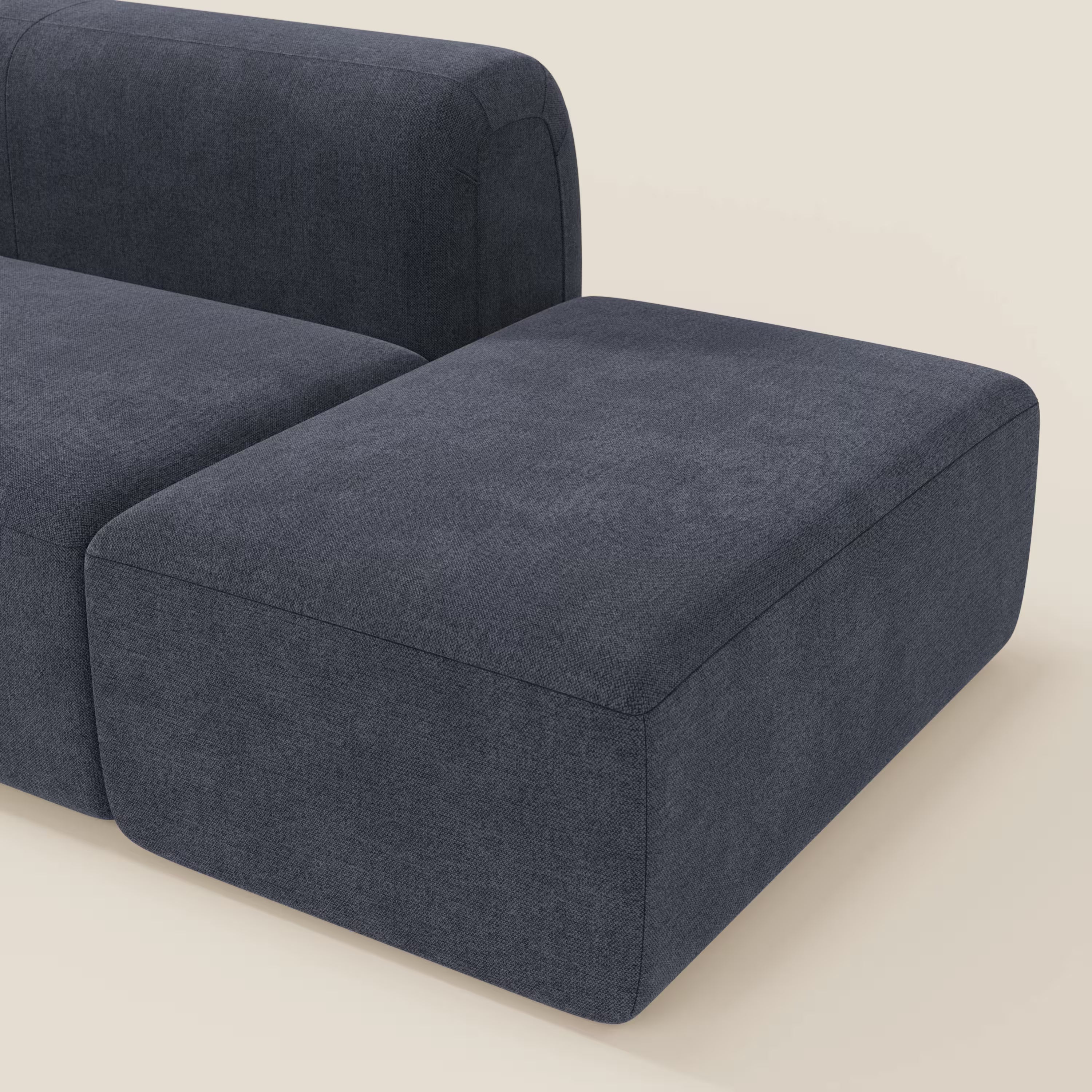 Primo piano di BonBon Divano componibile di Divani.Store in tessuto smacchiabile T23 blu ardesia, dalle linee pulite e dal design minimalista, con il pouf terminale posizionato di fronte su uno sfondo beige chiaro.