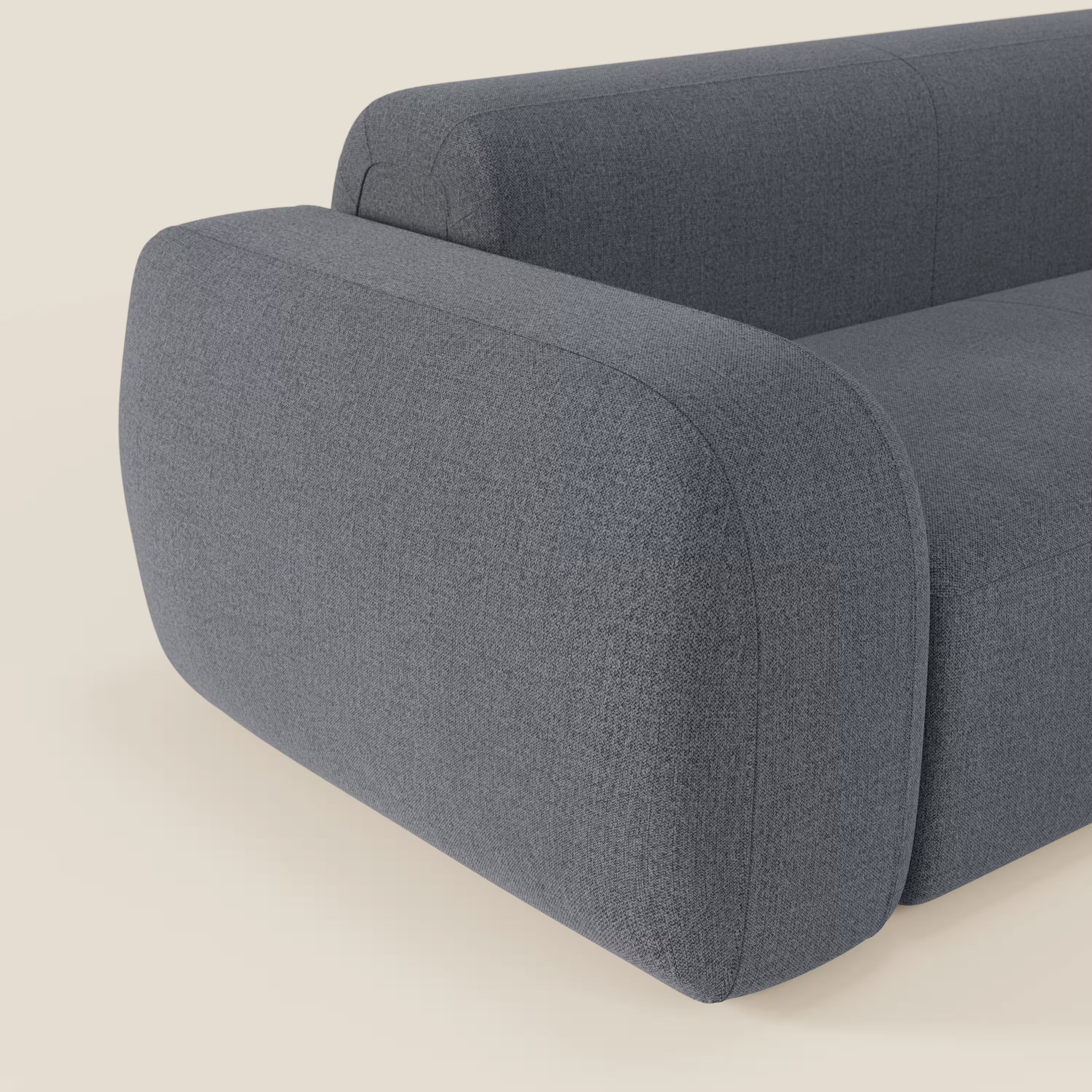Un primo piano del BonBon Divano componibile - Composizione con pouf terminale in tessuto smacchiabile T23 blu grafite di Divani.Store, caratterizzato da bordi arrotondati e cuscini in peluche per un look accogliente e minimalista su uno sfondo neutro.