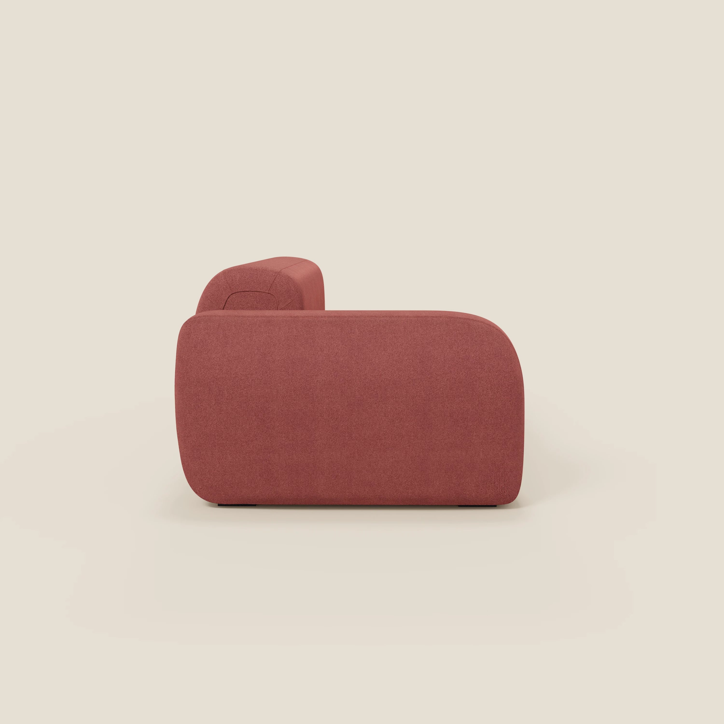 Il Divano componibile BonBon di Divani.Store, presentato di lato su uno sfondo beige chiaro, è caratterizzato da braccioli e schienale spessi e curvi in tessuto T23 rosso ciliegia, facile da pulire, per un look elegante e moderno.