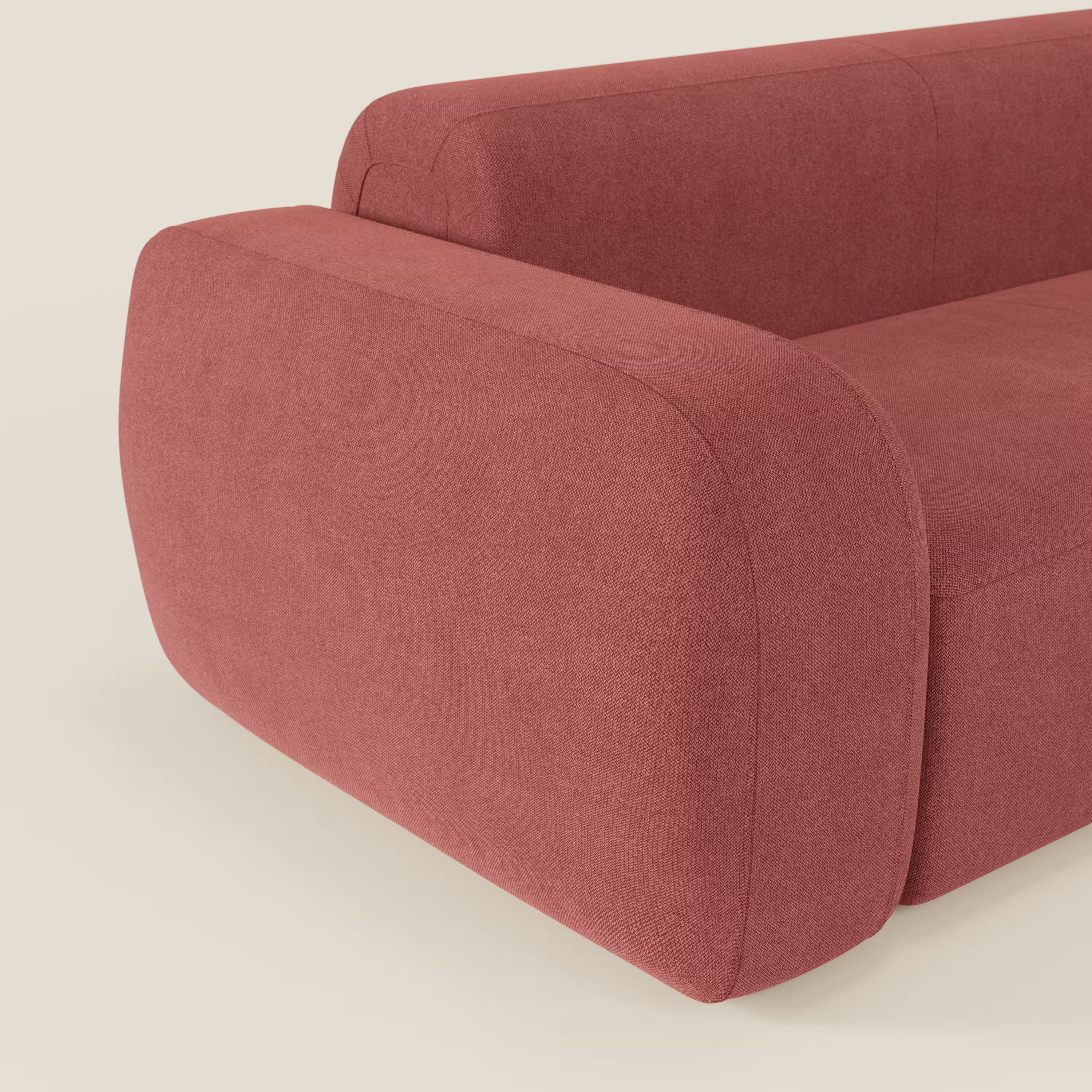 Un primo piano del BonBon Divano componibile - Composizione con pouf terminale di Divani.Store in tessuto smacchiabile T23 rosso ciliegia, che mostra il bracciolo arrotondato, le curve morbide e il design minimalista su uno sfondo crema chiaro.