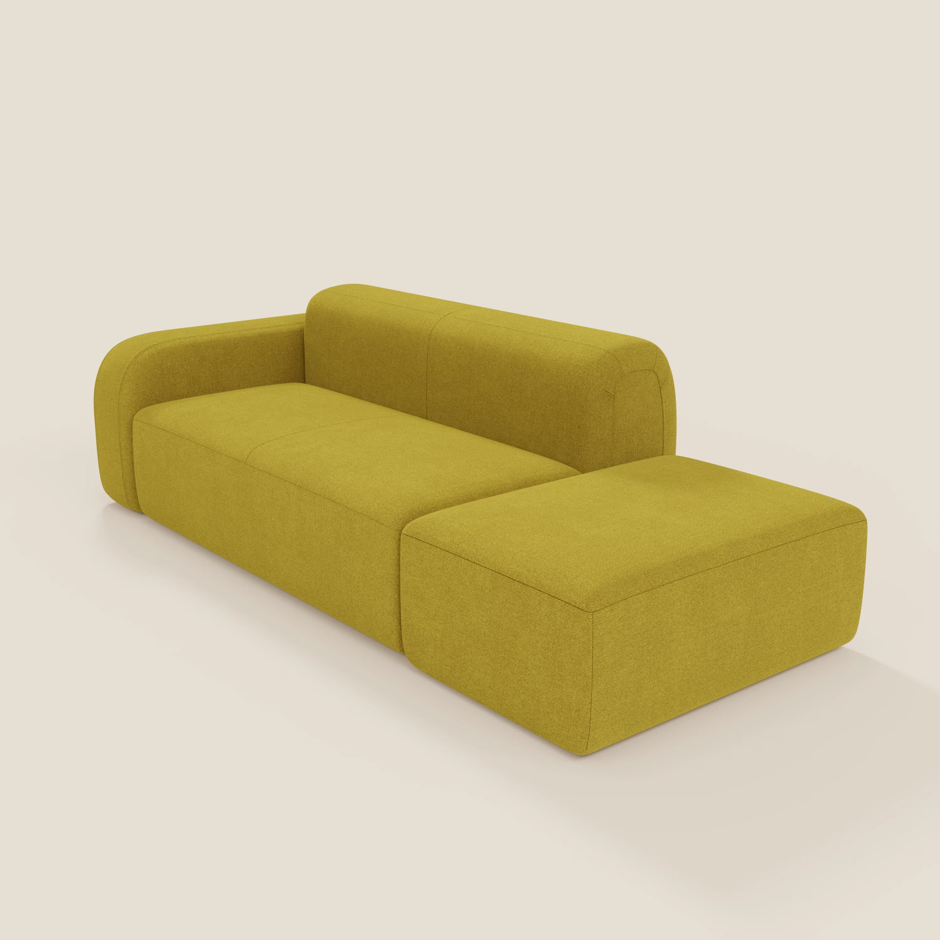 Il BonBon Divano componibile di Divani.Store, in smacchiabile suola T23 giallo, presenta un design moderno con curve morbide e una chaise lounge con braccio sinistro e pouf terminale, che si staglia su uno sfondo bianco sporco.