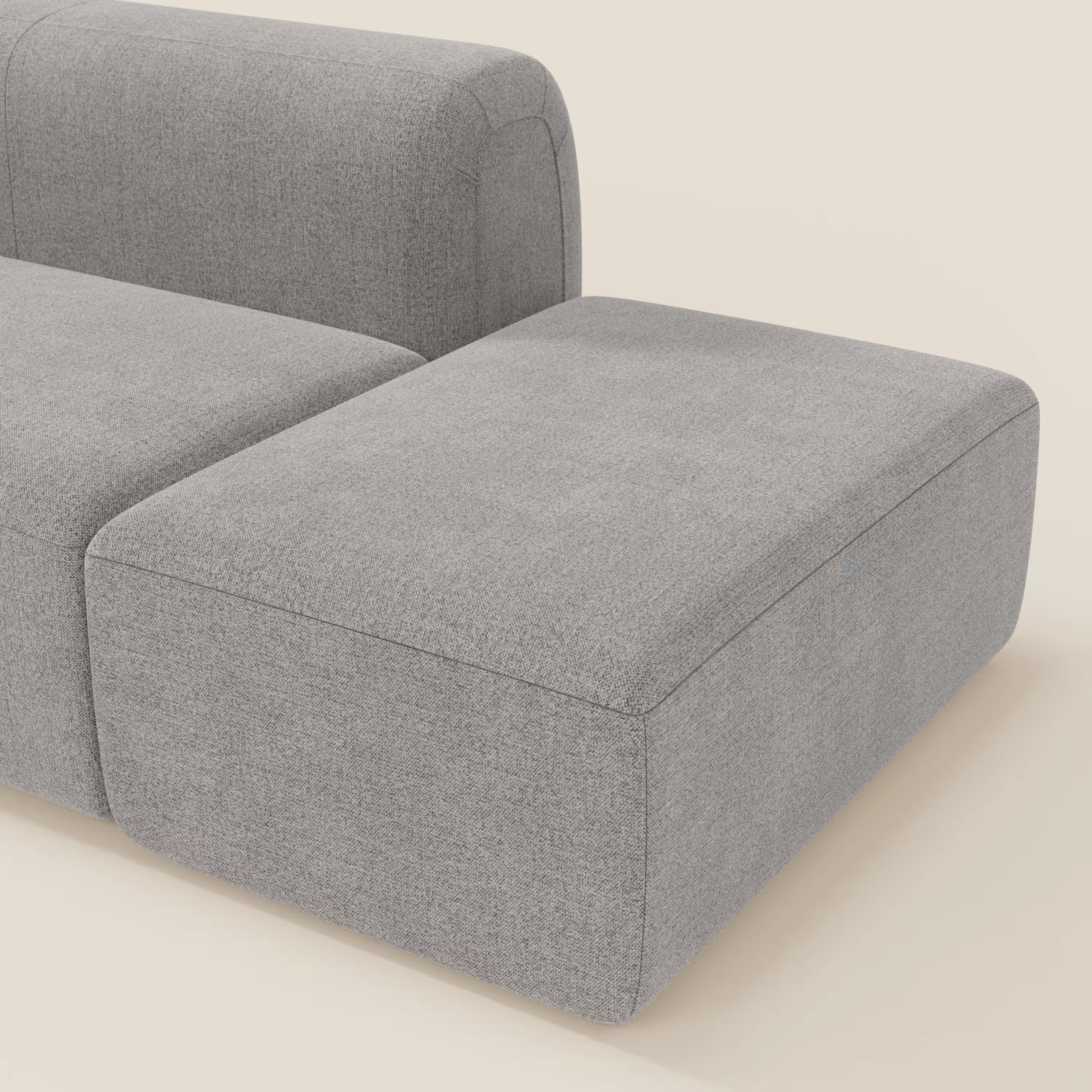 Vista dettagliata del divano componibile BonBon Divano di Divani.Store, in tessuto antimacchia T23 grigio con pouf terminale, caratterizzato da linee pulite e stile minimalista su uno sfondo beige chiaro. Sono visibili solo parte dello schienale, della seduta e del pouf.
