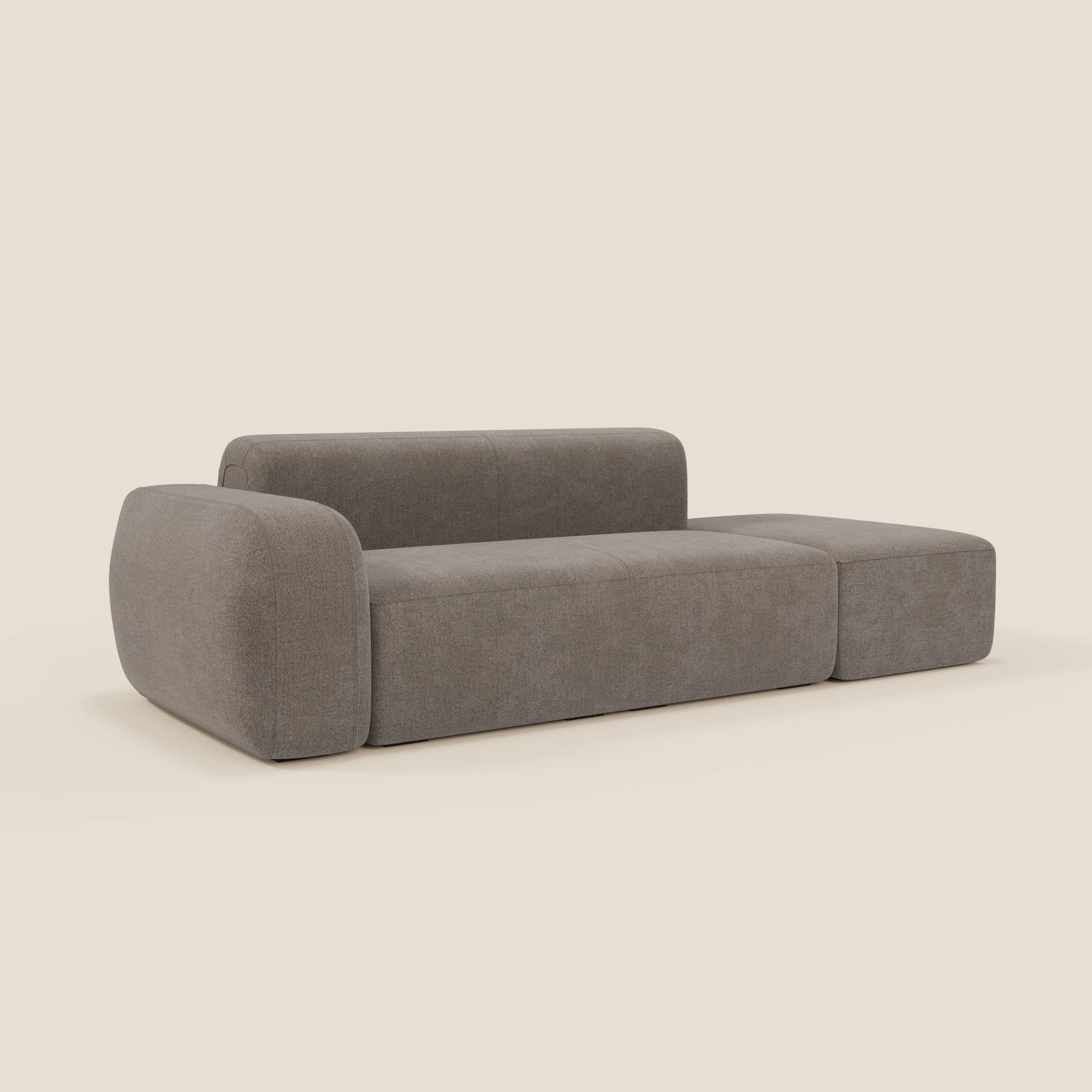 Il BonBon Divano componibile di Divani.Store in smacchiabile T23 talpa è caratterizzato da un design minimalista con una seduta spessa, uno schienale coordinato, un bracciolo arrotondato e un pouf terminale: la sua silhouette semplice spicca su uno sfondo beige chiaro.
