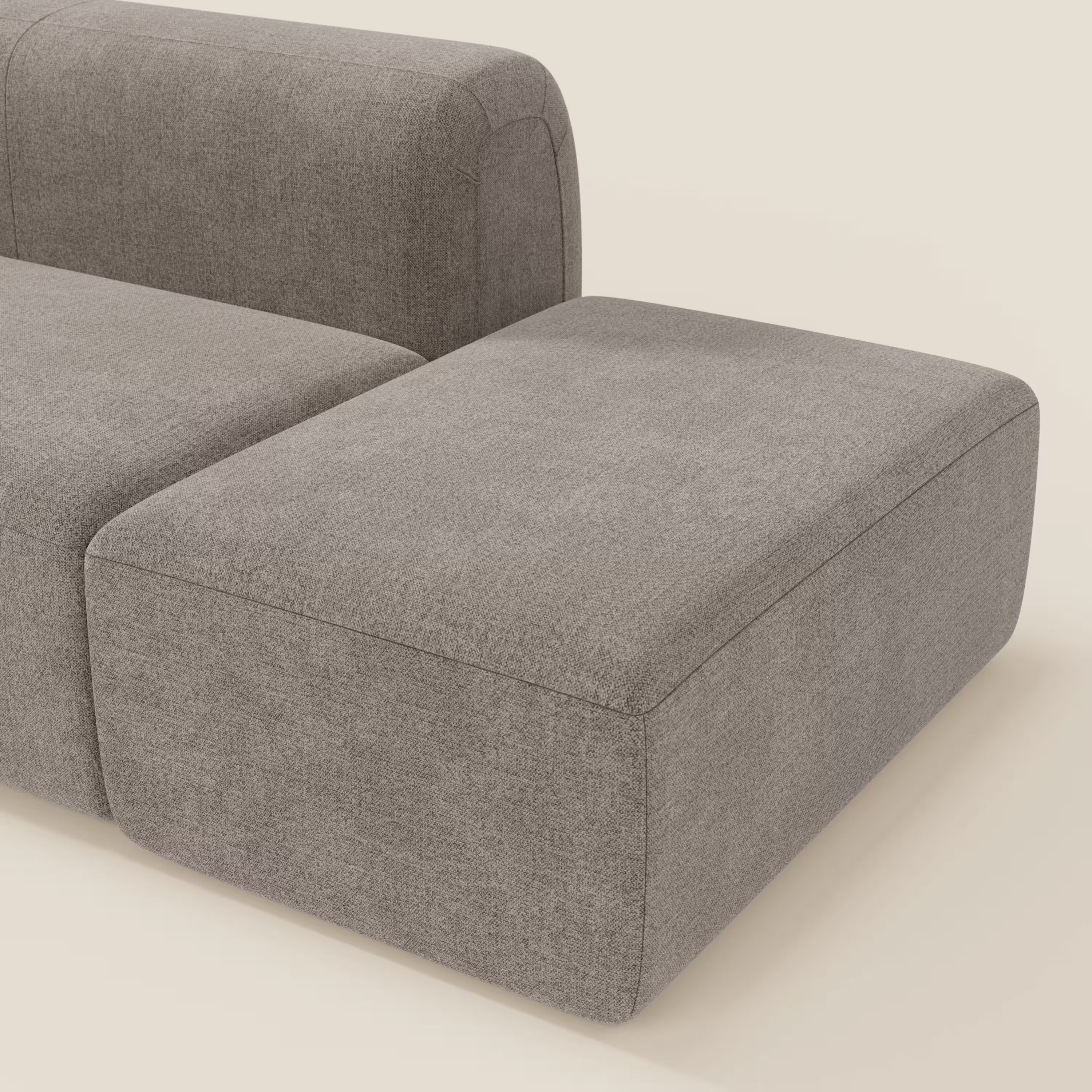 Un moderno pouf terminale rettangolare grigio del BonBon Divano componibile di Divani.Store si affianca al divano coordinato. Entrambi hanno bordi lisci e arrotondati e un design minimalista, su uno sfondo beige chiaro per un look contemporaneo.