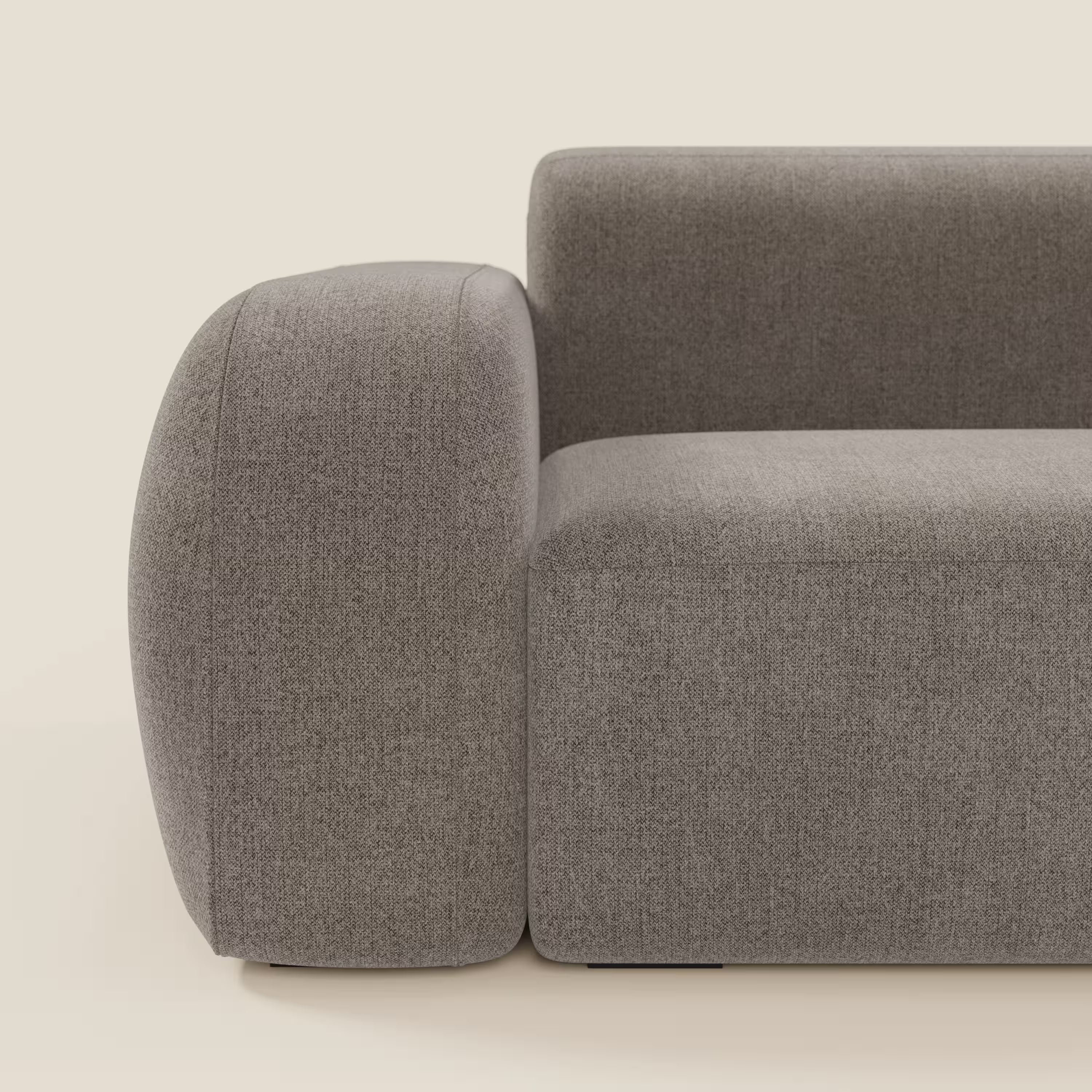 Vista laterale ravvicinata del divano componibile BonBon Divano di Divani.Store, in tessuto smacchiabile T23 talpa, con bracciolo e schienale arrotondati, linee pulite e imbottitura morbida, su sfondo beige chiaro.