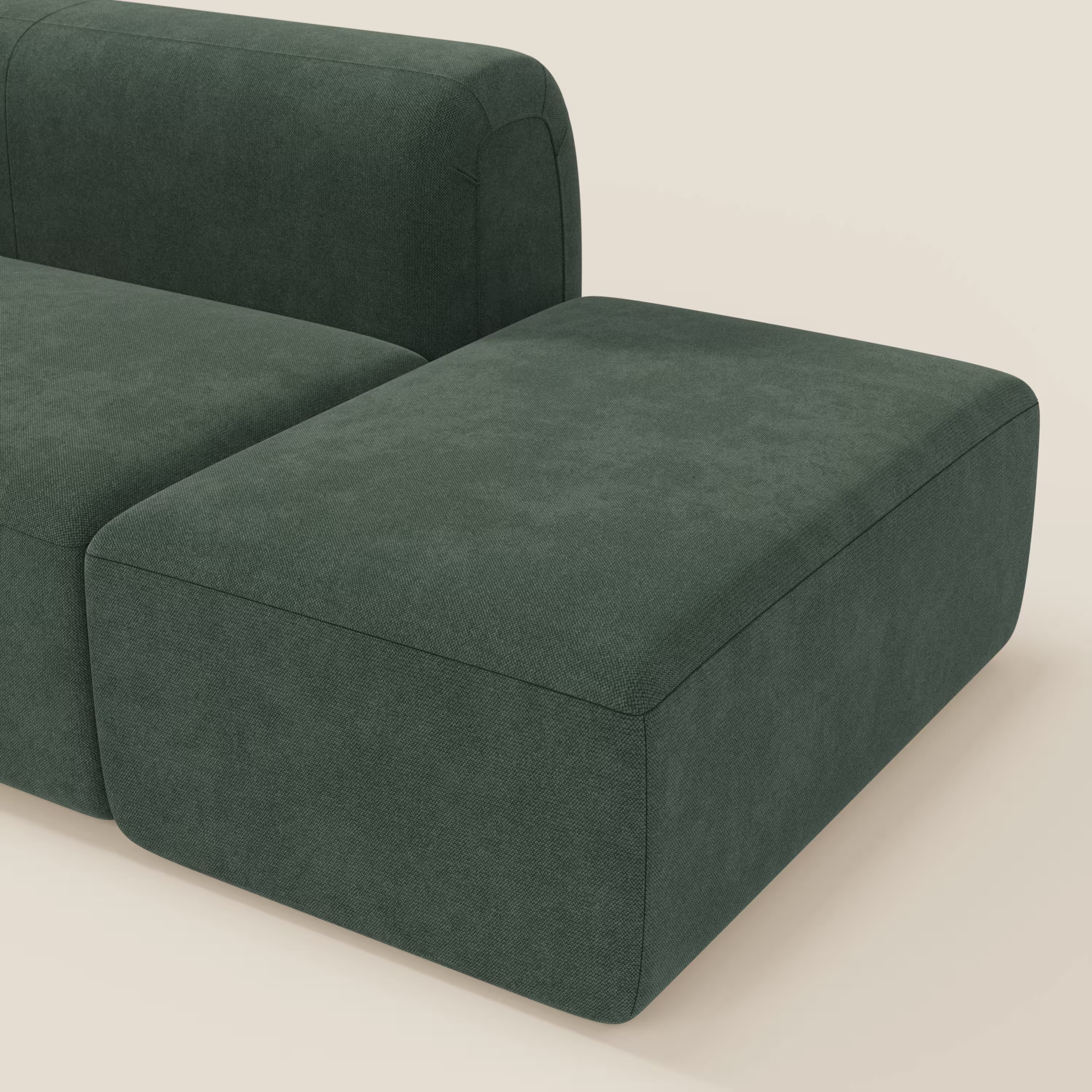 Il BonBon Divano componibile di Divani.Store in tessuto smacchiabile T23 verde è caratterizzato da un design basso e squadrato con bordi arrotondati, sezione angolare e pouf terminale, presentato su uno sfondo neutro color crema.