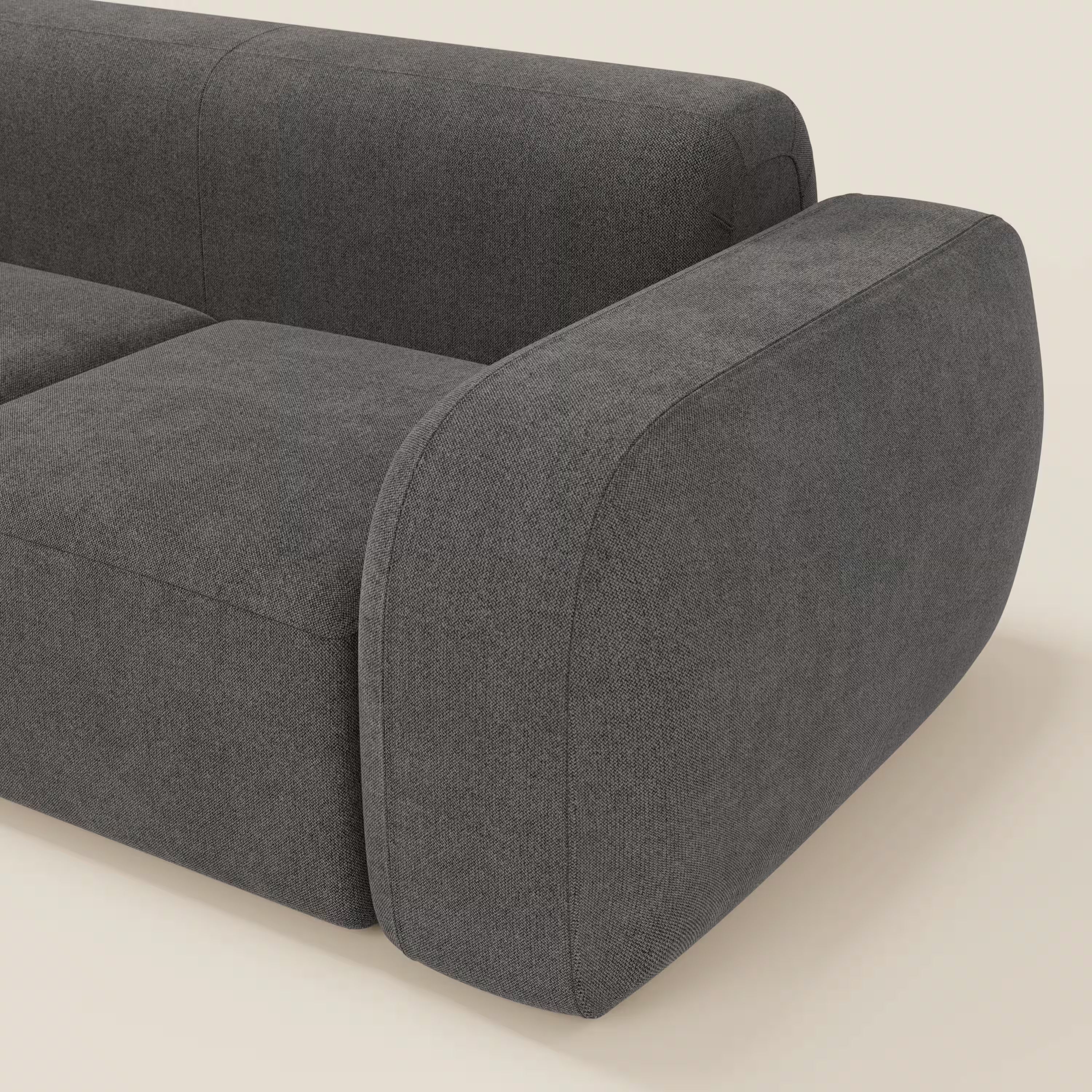 Primo piano di BonBon Divano modulare componibile - Composizione Spaccamattone di Divani.Store, in tessuto smacchiabile T23 antracite, con ampio bracciolo arrotondato e cuscini in feltro, su sfondo beige chiaro.