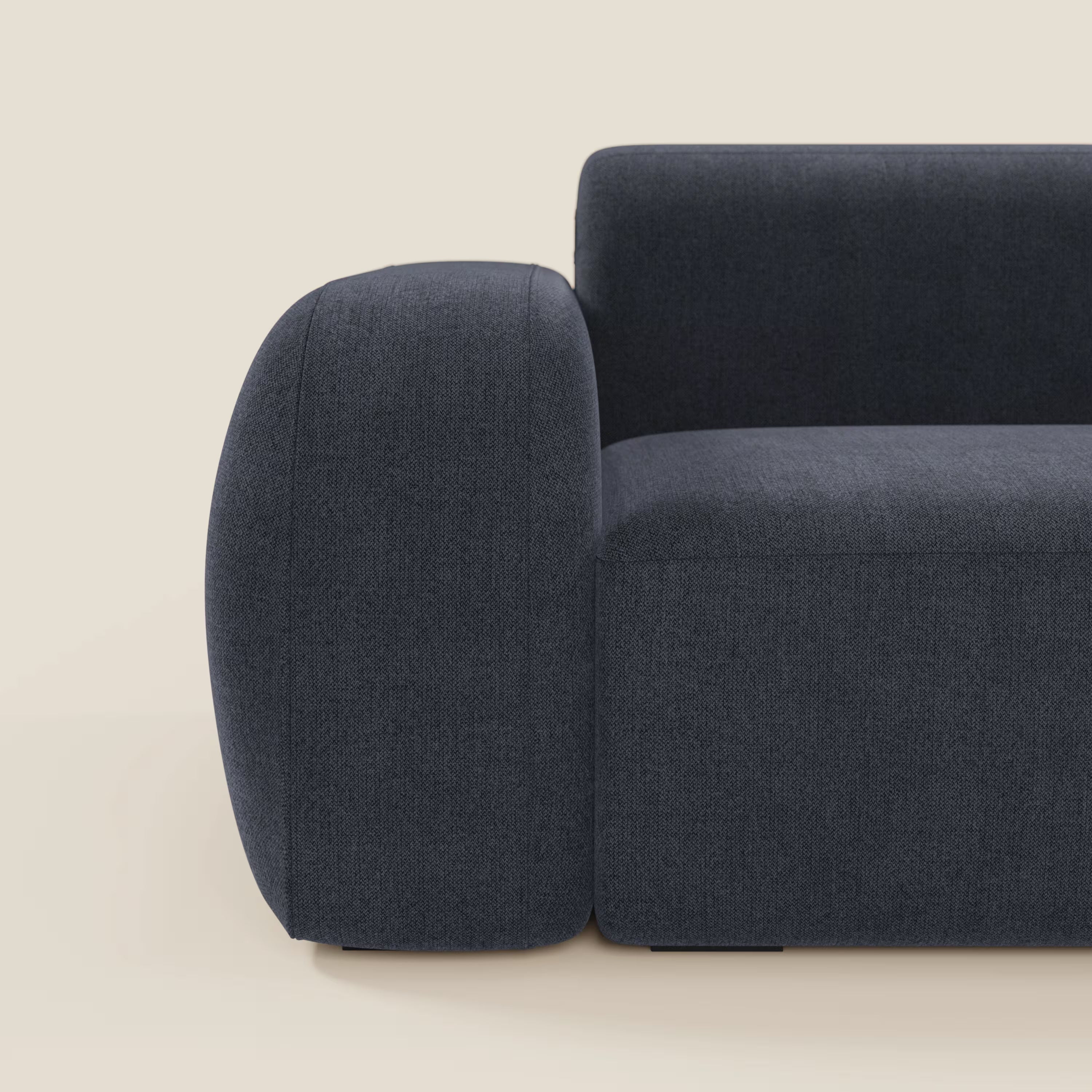 Primo piano del lato sinistro di BonBon Divano componibile - Composizione Spaccamattone in tessuto smacchiabile T23 blu ardesia di Divani.Store, che mostra il bracciolo e lo schienale arrotondati su uno sfondo beige chiaro. È visibile solo una parte della seduta.