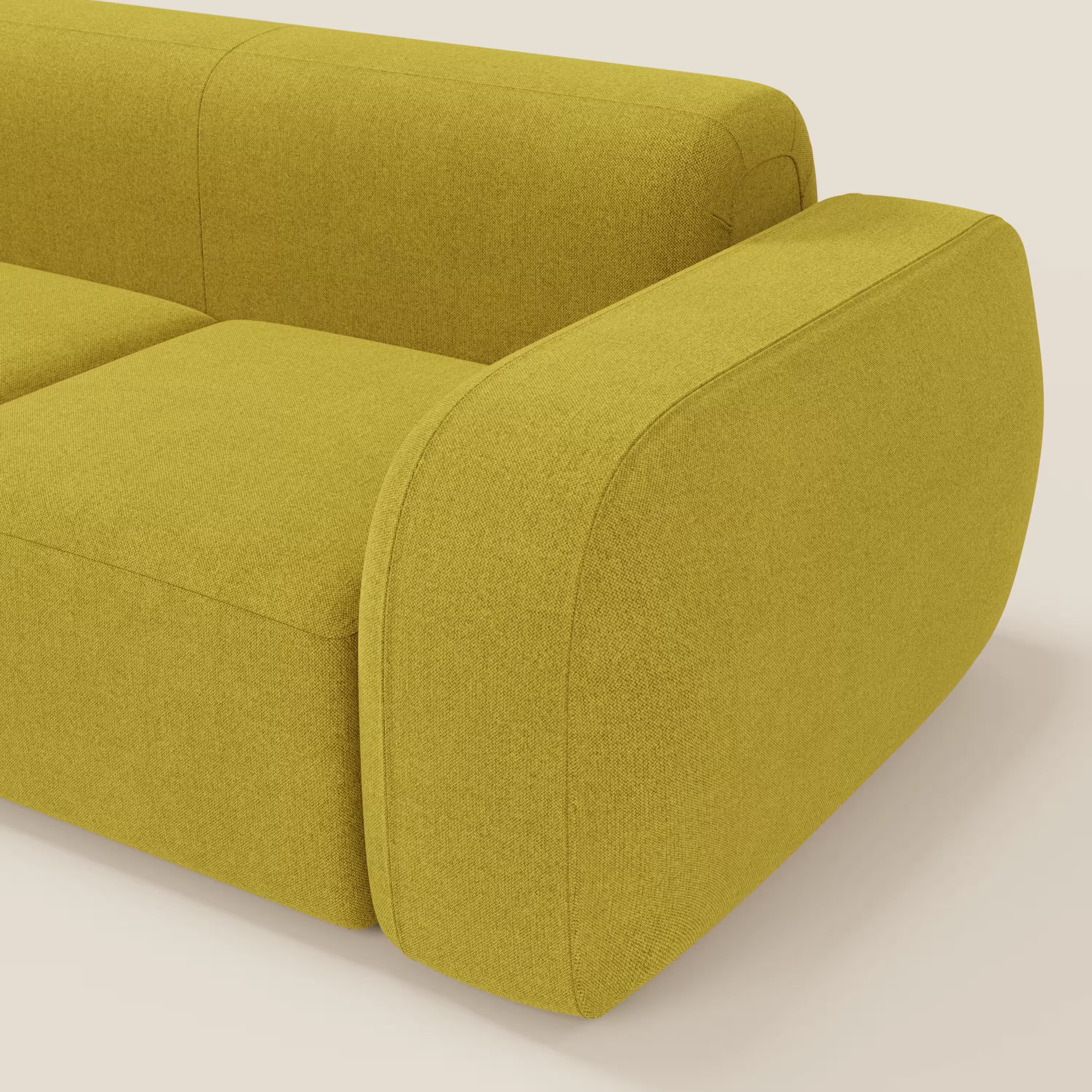 Primo piano del divano componibile BonBon Divano - Composizione Spaccamattone di Divani.Store, in tessuto antimacchia T23 giallo, con braccioli spessi e arrotondati e cuscini morbidi su uno sfondo beige chiaro.