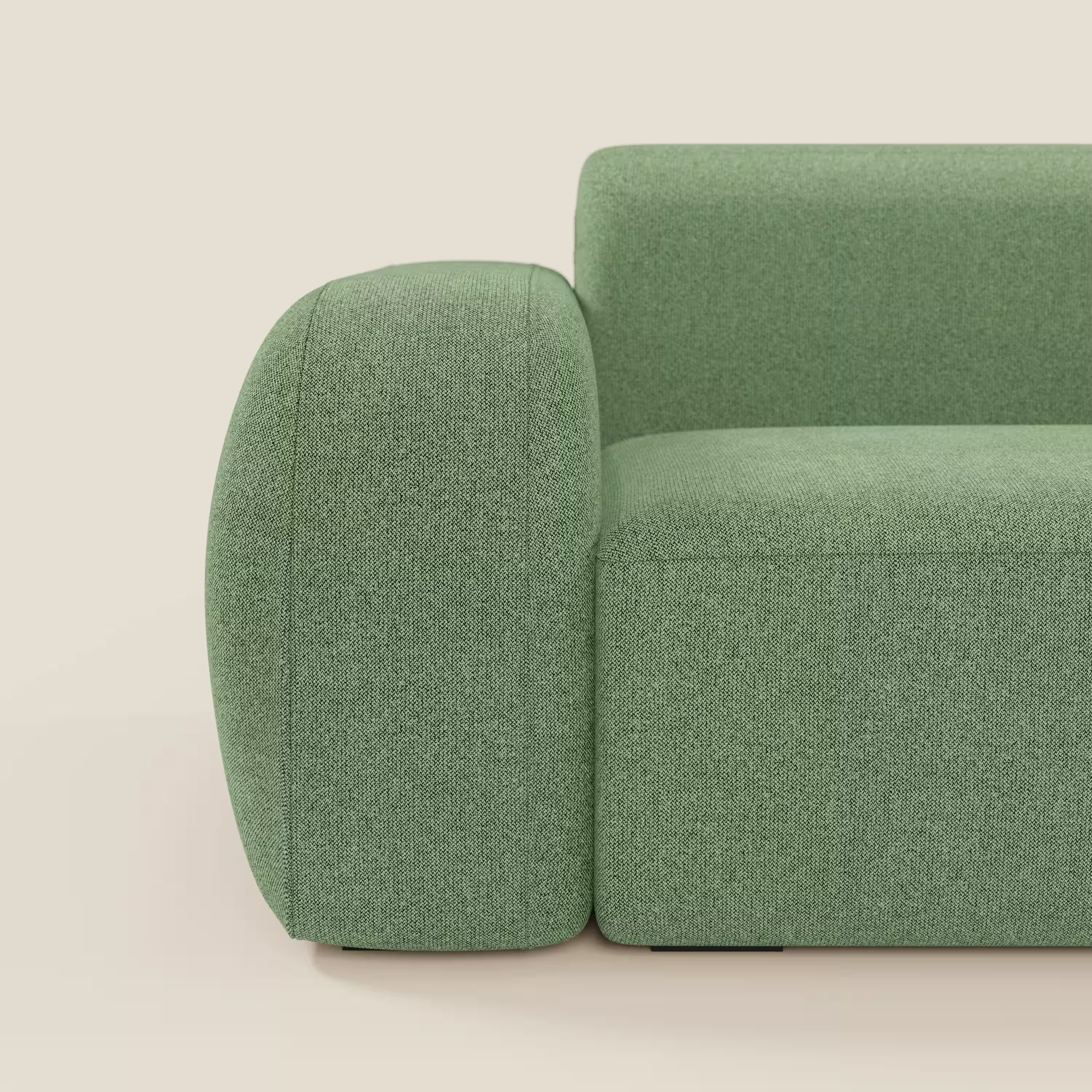 Primo piano del divano componibile BonBon Divano - Composizione Spaccamattone di Divani.Store in tessuto menta T23, facile da pulire, caratterizzato da bordi morbidi e arrotondati e da un design minimalista e felpato con bracciolo e seduta in primo piano su uno sfondo chiaro.