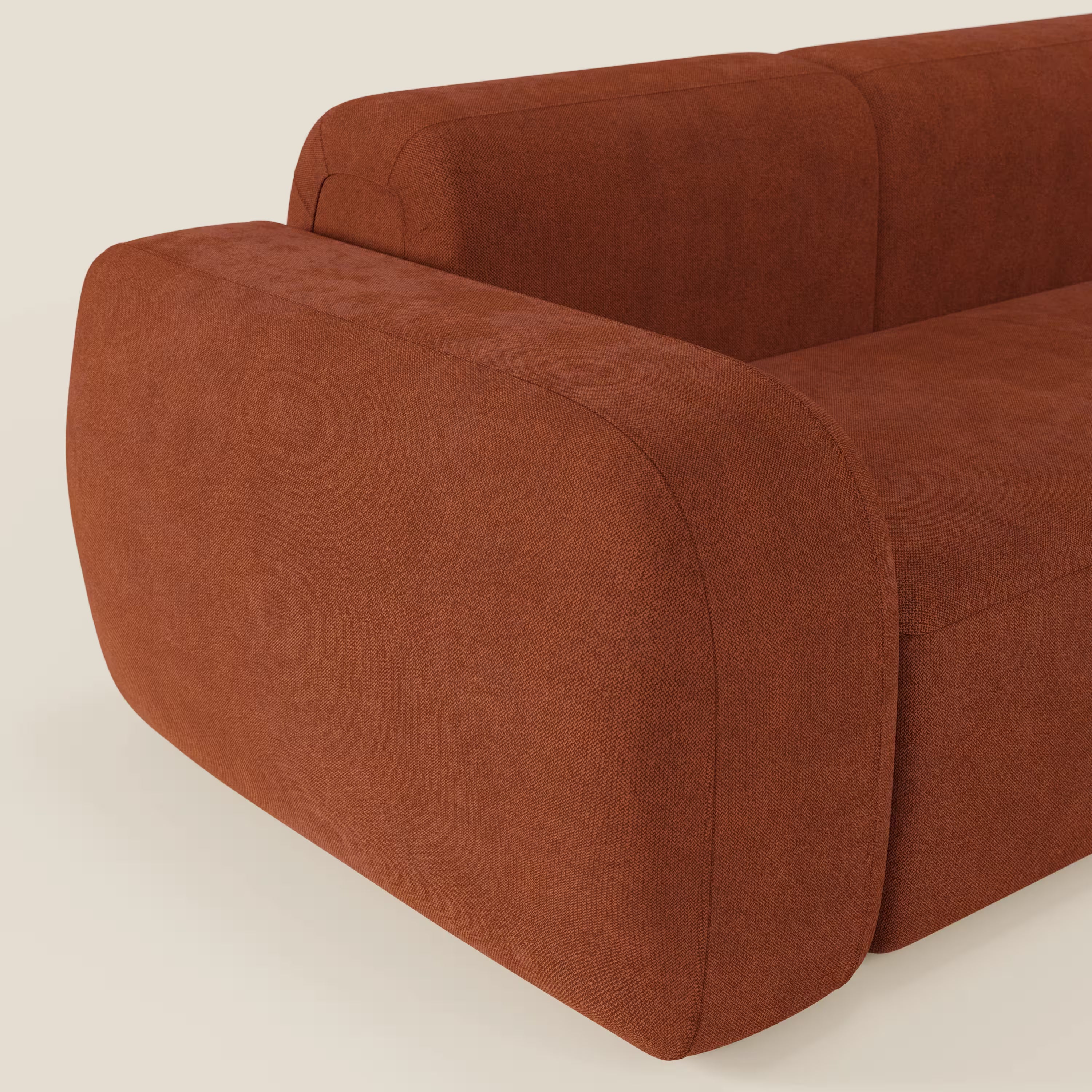 Un primo piano mette in evidenza il BonBon Divano componibile - Composizione Spaccamattone di Divani.Store, caratterizzato da bordi arrotondati e braccioli spessi in tessuto ruggine T23 antimacchia, su uno sfondo beige chiaro.