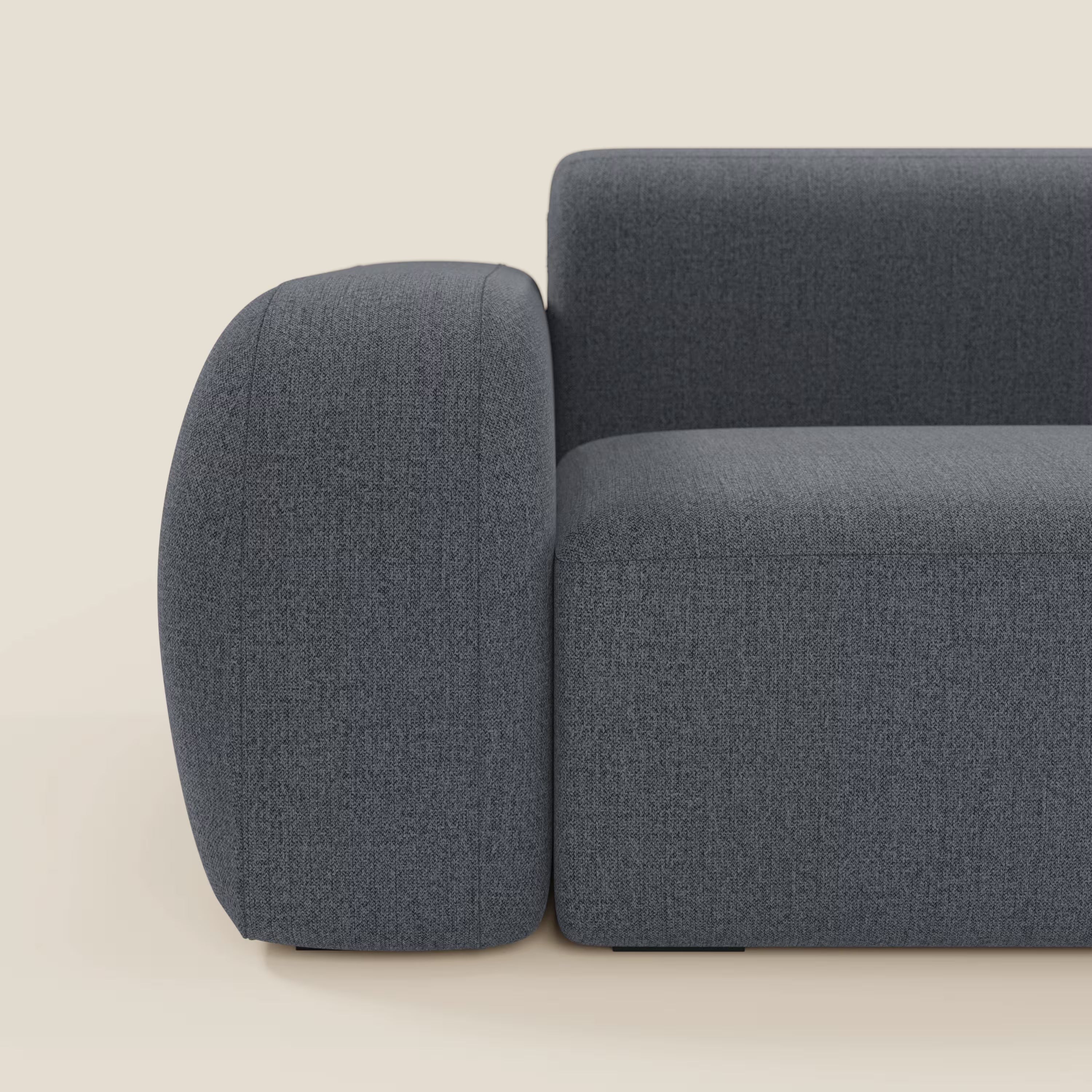 Il divano BonBon angolare componibile e modulare di Divani.Store è caratterizzato da braccioli spessi e arrotondati e da uno schienale in tessuto grafite T23 blu antimacchia. In figura, il braccio sinistro e il cuscino della seduta su uno sfondo chiaro.