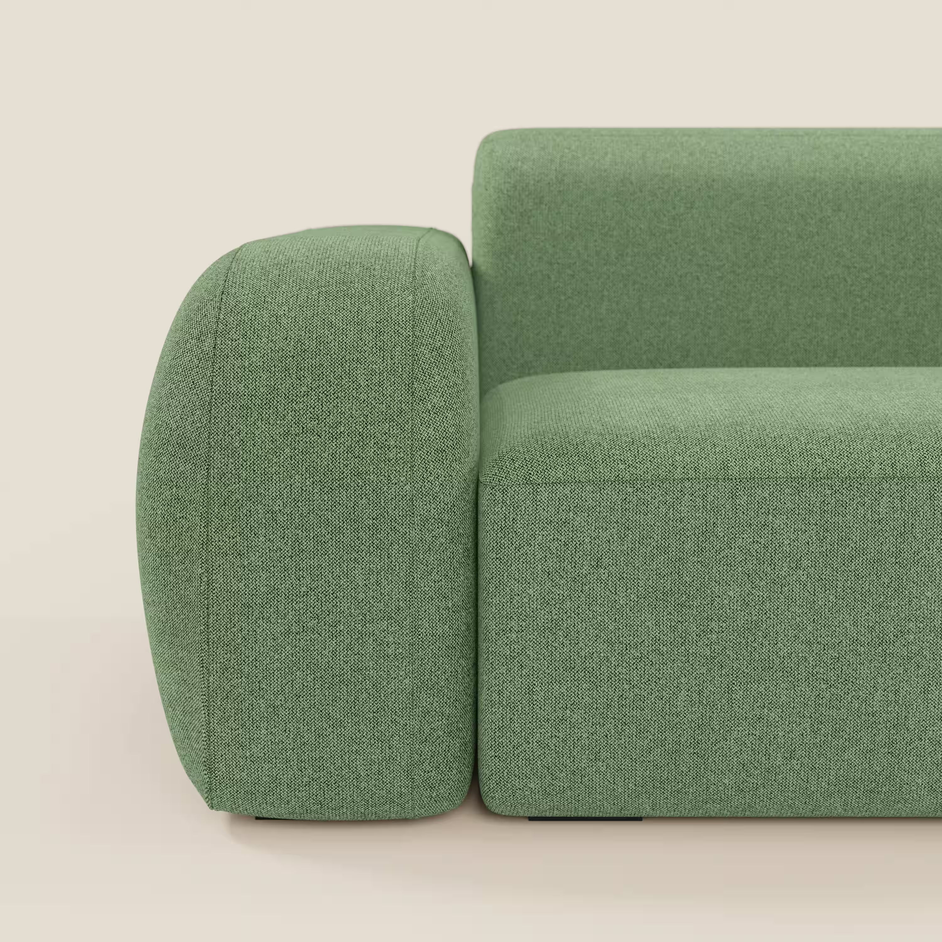 Primo piano del divano angolare componibile e modulare BonBon di Divani.Store in tessuto smacchiabile T23 menta, caratterizzato da braccioli spessi e arrotondati e da linee pulite, presentato su un pavimento chiaro con sfondo bianco sporco.