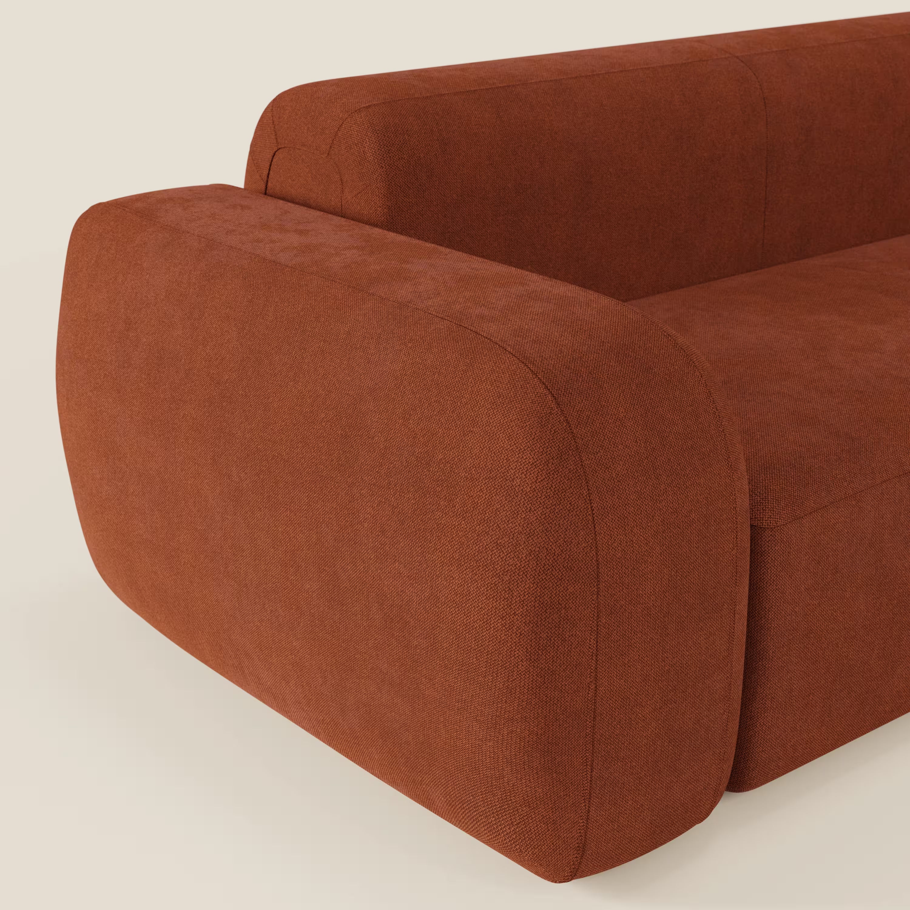 Primo piano del divano angolare componibile e modulare BonBon di Divani.Store, rivestito in tessuto antimacchia T23 ruggine. I braccioli ampi e arrotondati e le curve morbide creano un'atmosfera contemporanea su uno sfondo bianco sporco.