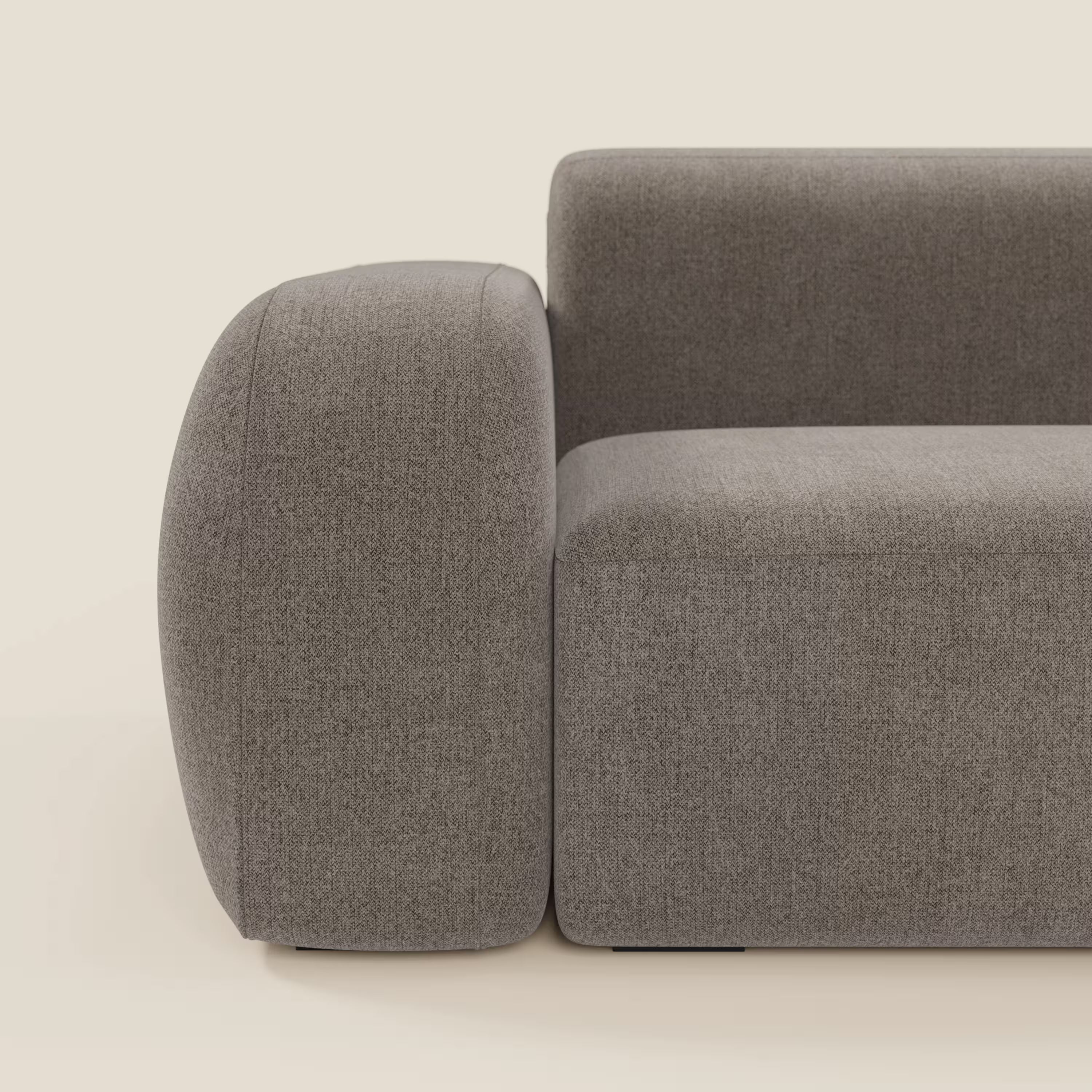 Primo piano laterale del divano angolare componibile e modulare BonBon di Divani.Store, caratterizzato da bordi morbidi e arrotondati, bracciolo spesso e tessuto smacchiabile T23 talpa. Lo sfondo beige semplice ne evidenzia il design pulito e contemporaneo.