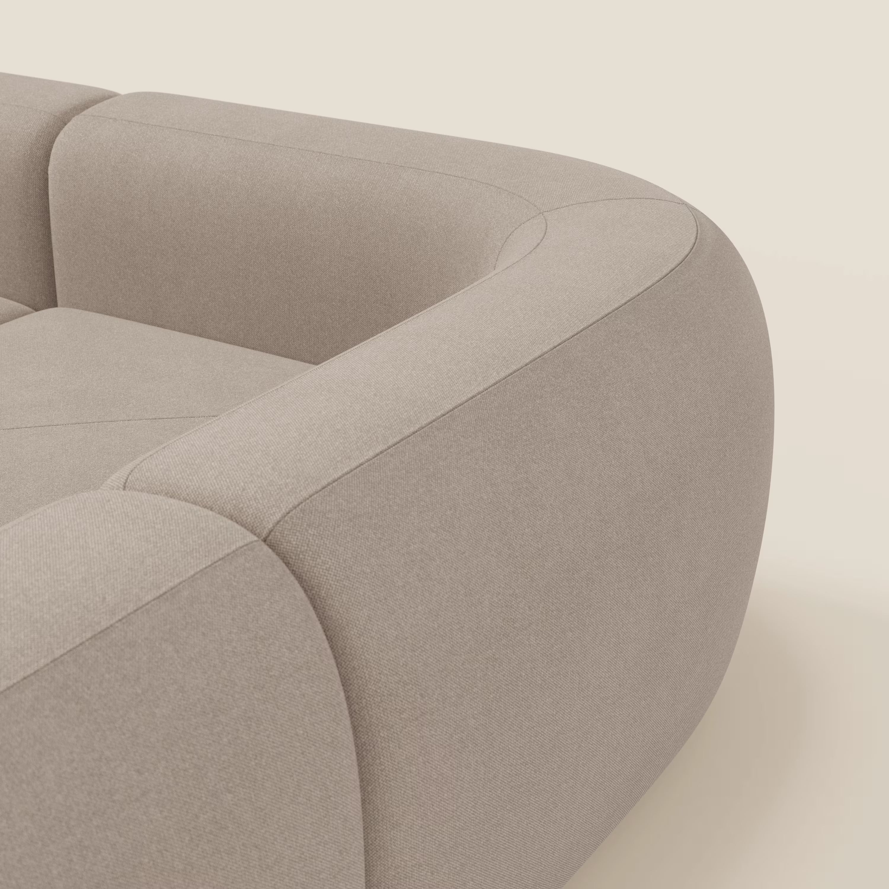 Un primo piano del divano angolare componibile e modulare BonBon di Divani.Store in tessuto tortora T23, beige chiaro e antimacchia, mostra i suoi bordi arrotondati, l'imbottitura morbida e il design minimalista su uno sfondo morbido.