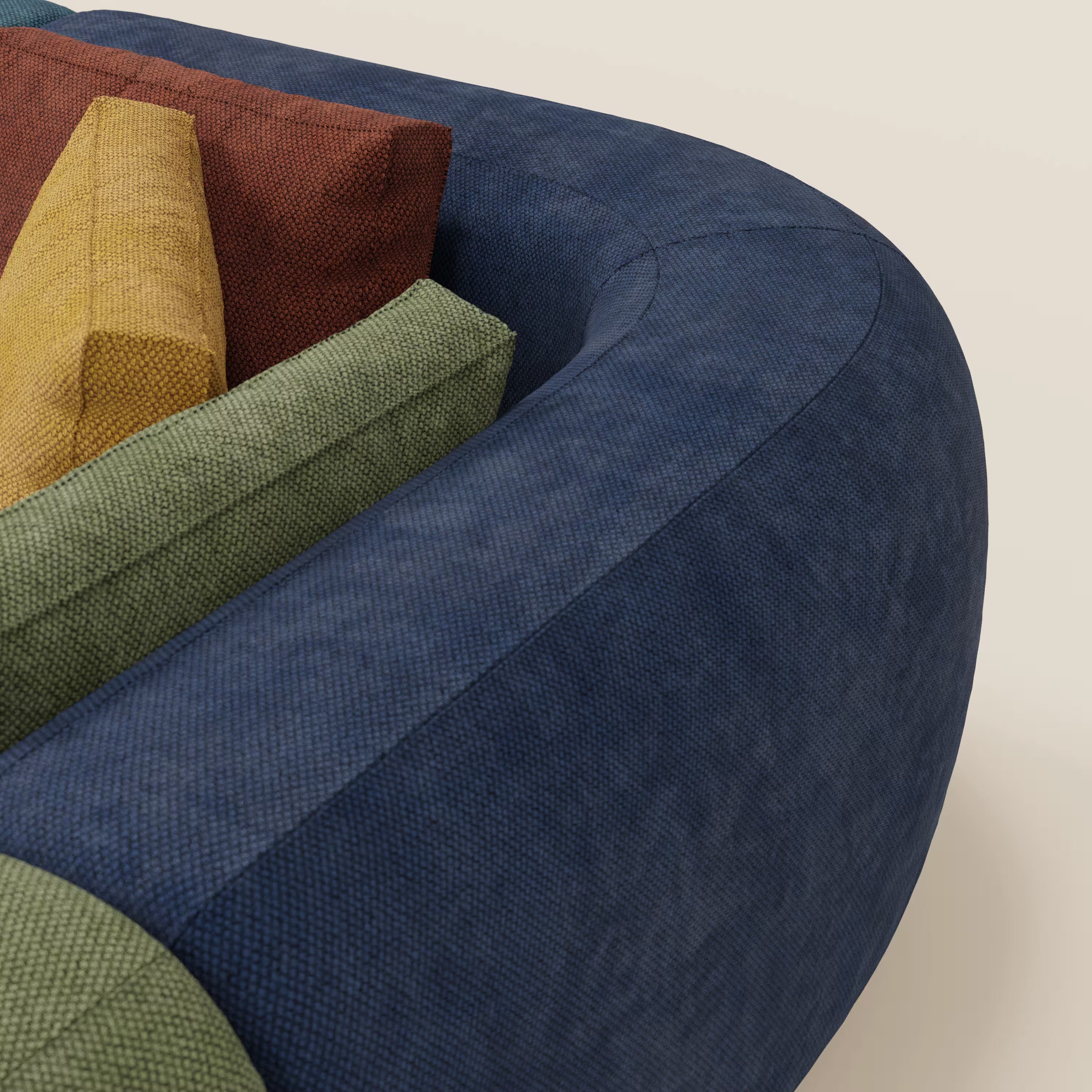 Primo piano del divano componibile angolare BonBon - Grande Fratello Edition di Divani.Store, caratterizzato da un tessuto strutturato blu scuro, uno spesso bracciolo arrotondato e cuscini rettangolari verdi, gialli e rosso ruggine su uno sfondo bianco sporco.