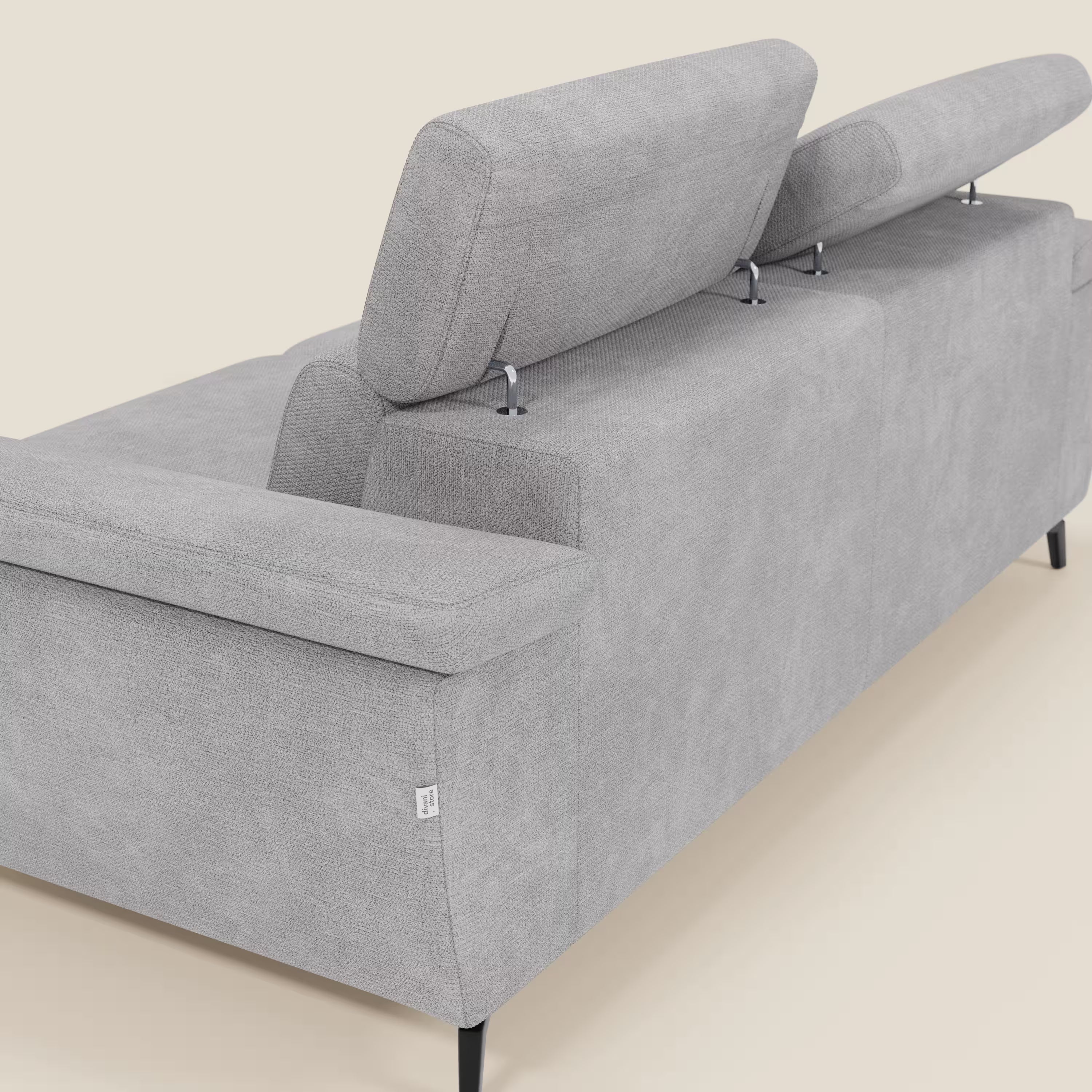 L'Estro Divano 3 posti con pouf estraibile di Divani.Store, in tessuto impermeabile T14 grigio chiaro, offre poggiatesta reclinabili, gambe sottili in metallo nero e braccioli rettangolari. Vista posteriore angolata su sfondo chiaro.
