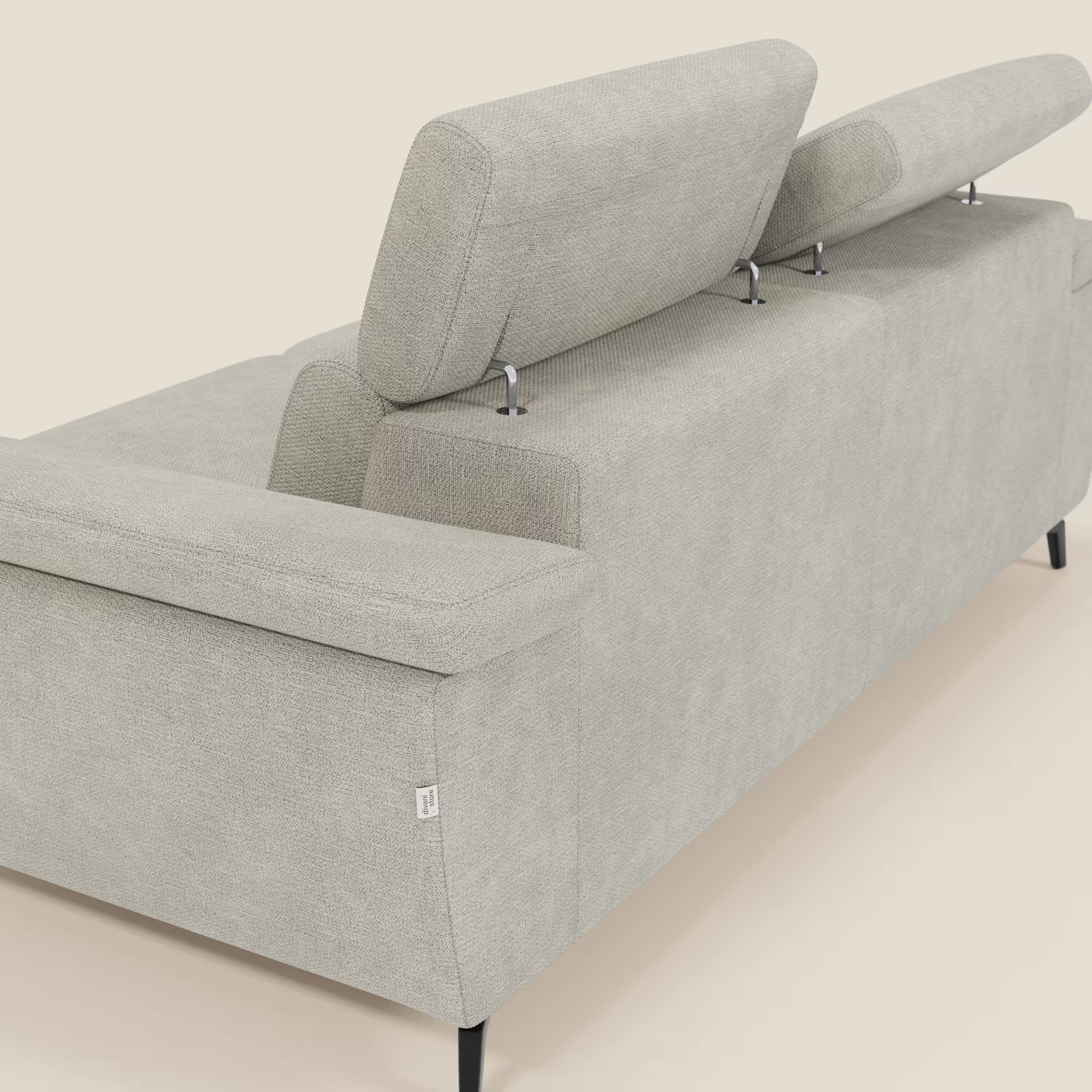 L'Estro Divano 3 posti con pouf estraibile di Divani.Store, in tessuto impermeabile T14 panna, è mostrato da dietro con poggiatesta reclinabili ad altezze diverse, linee moderne e gambe sottili nere su sfondo beige chiaro.