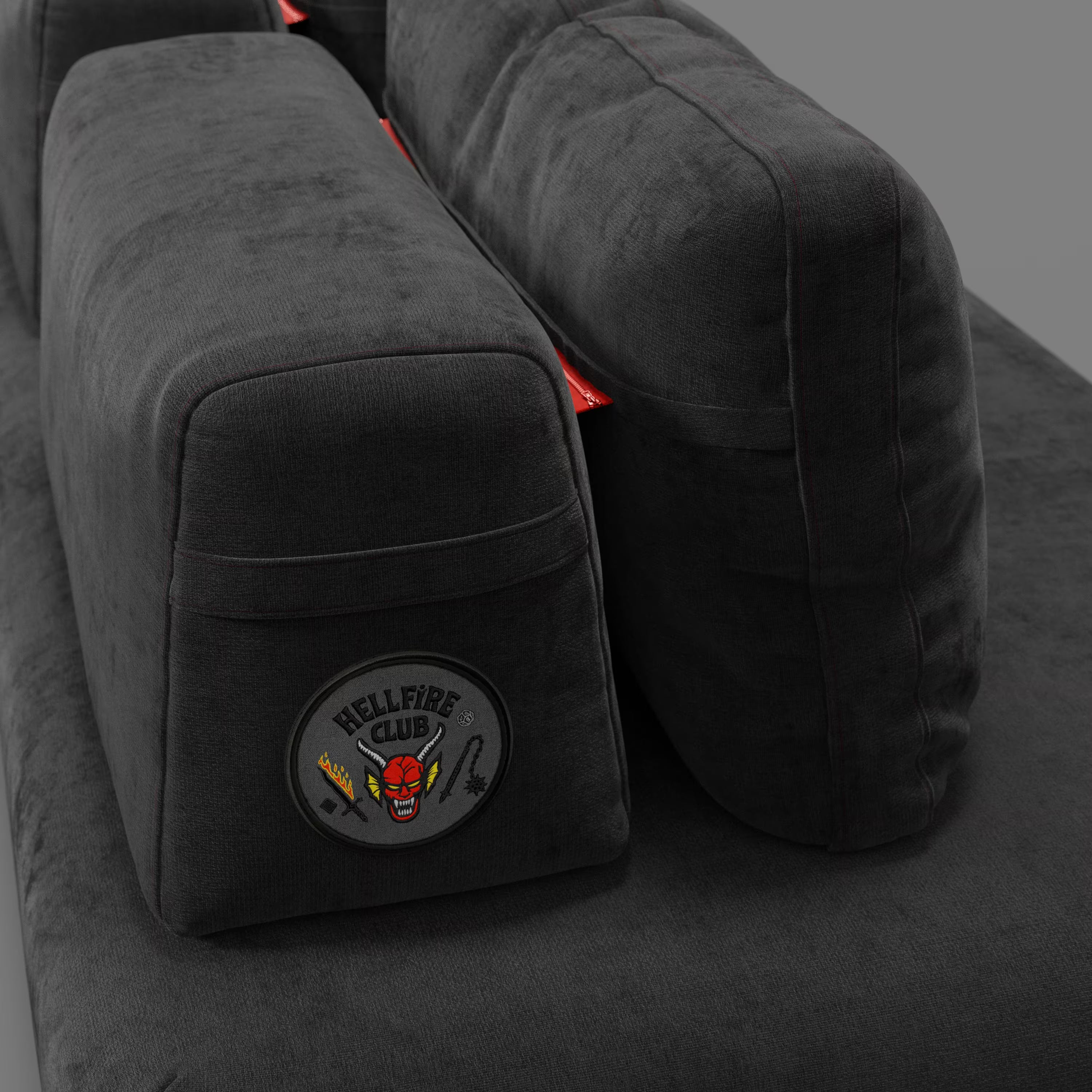 Un primo piano del Divani.Store Rift divano letto matrimoniale STRANGER THINGS Edition in smacchiabile antracite mostra due grandi cuscini del bracciolo, uno dei quali presenta una patch "Hellfire Club" con un volto di demone rosso, una spada e un flail.