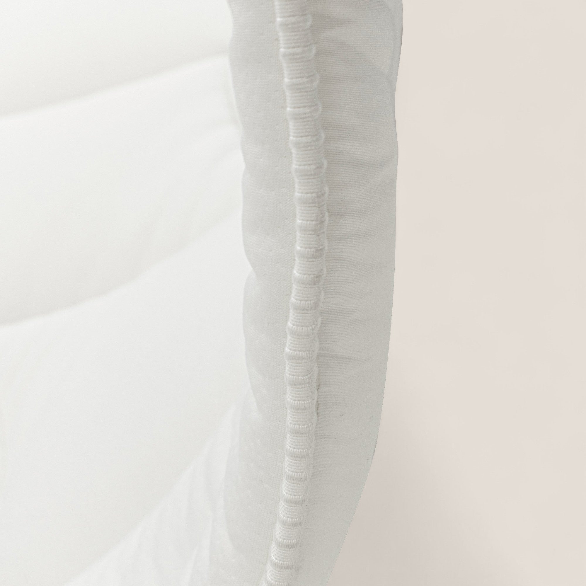 Primo piano del Topper Luxury KYROS-CLOUD in Memory Foam H5 cm con Tecnologia CoolMax di Divani.Store, che mostra il dettaglio delle cuciture curve lungo il bordo. Il design minimale e il tessuto bianco e pulito sono messi in risalto su uno sfondo morbido.