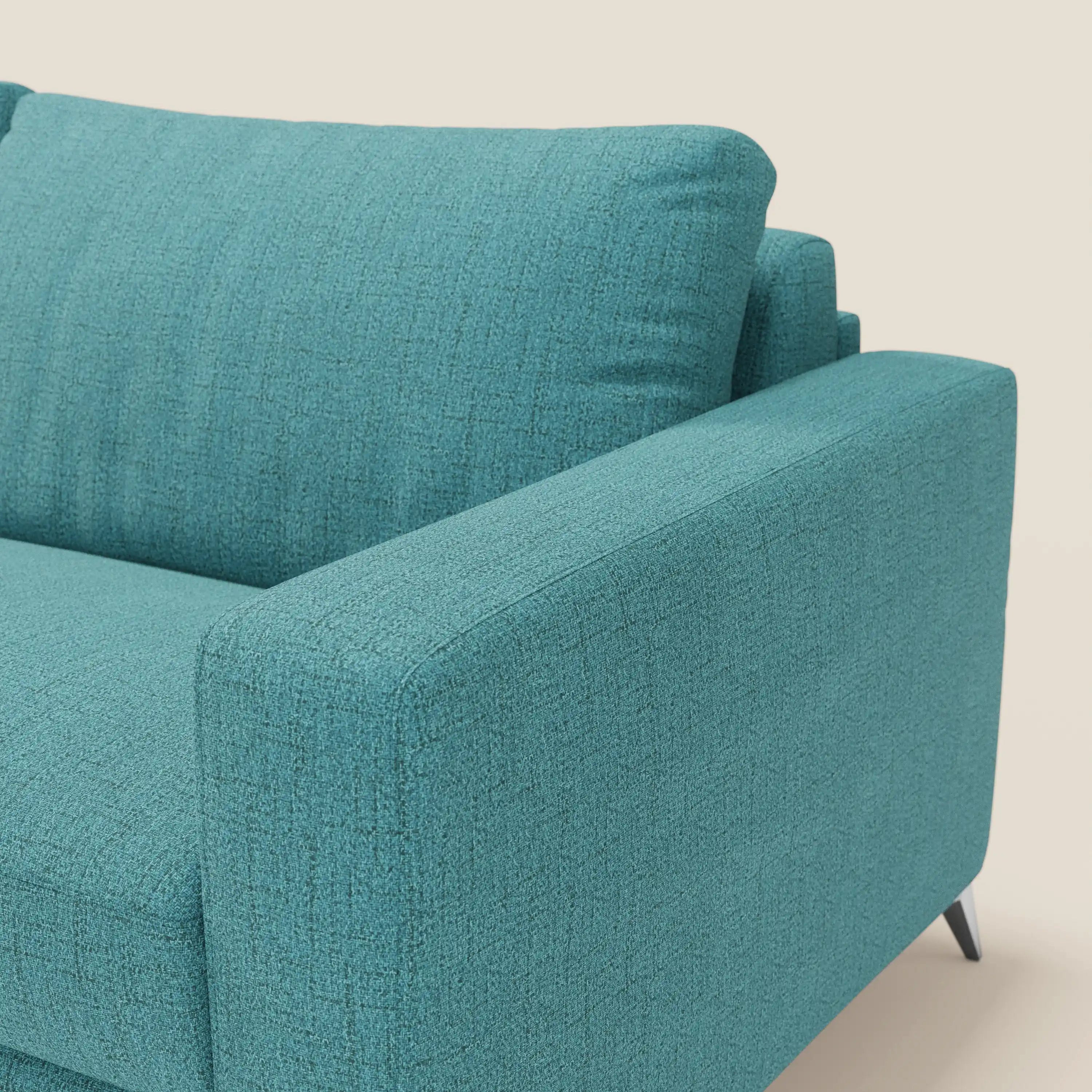 Primo piano del letto matrimoniale Alaya Divano di Divani.Store in tessuto impermeabile T03 azzurro, caratterizzato da morbidi cuscini e design minimale. L'inquadratura si concentra su bracciolo, seduta, cuscini dello schienale e sottili gambe nere su uno sfondo beige chiaro.