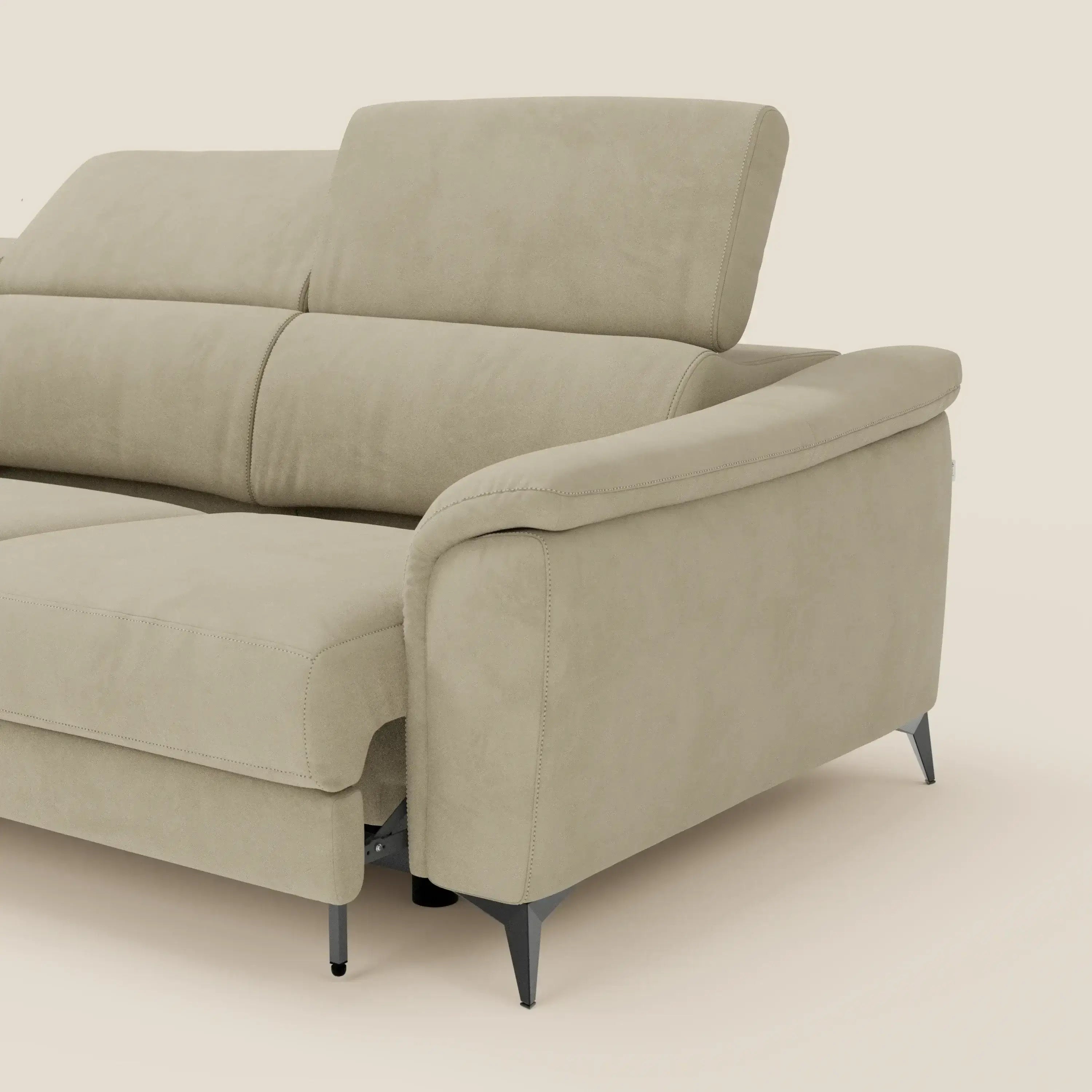 Un primo piano dell'Arcos Divano con penisola di Divani.Store in microfibra impermeabile T11 beige, con gambe alte e poggiatesta reclinabile, si concentra sul bracciolo e sulla zona di seduta su uno sfondo crema.