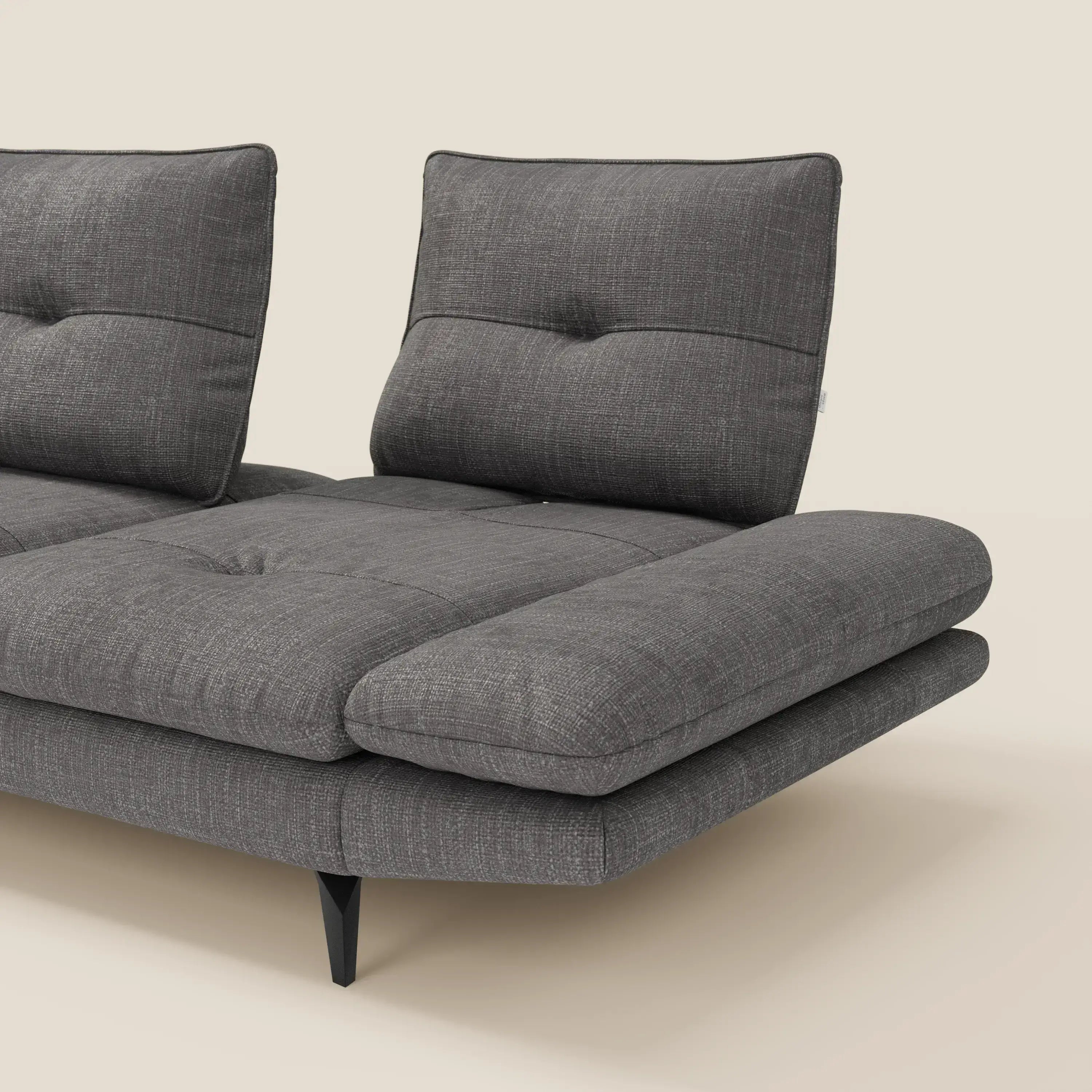 L'Ardex Divano con penisola di Divani.Store, presentato in tessuto impermeabile T06 antracite, è caratterizzato da schienali scorrevoli e braccioli regolabili. Il suo design moderno comprende cuscini trapuntati, gambe angolari nere e una chaise lounge parzialmente visibile.