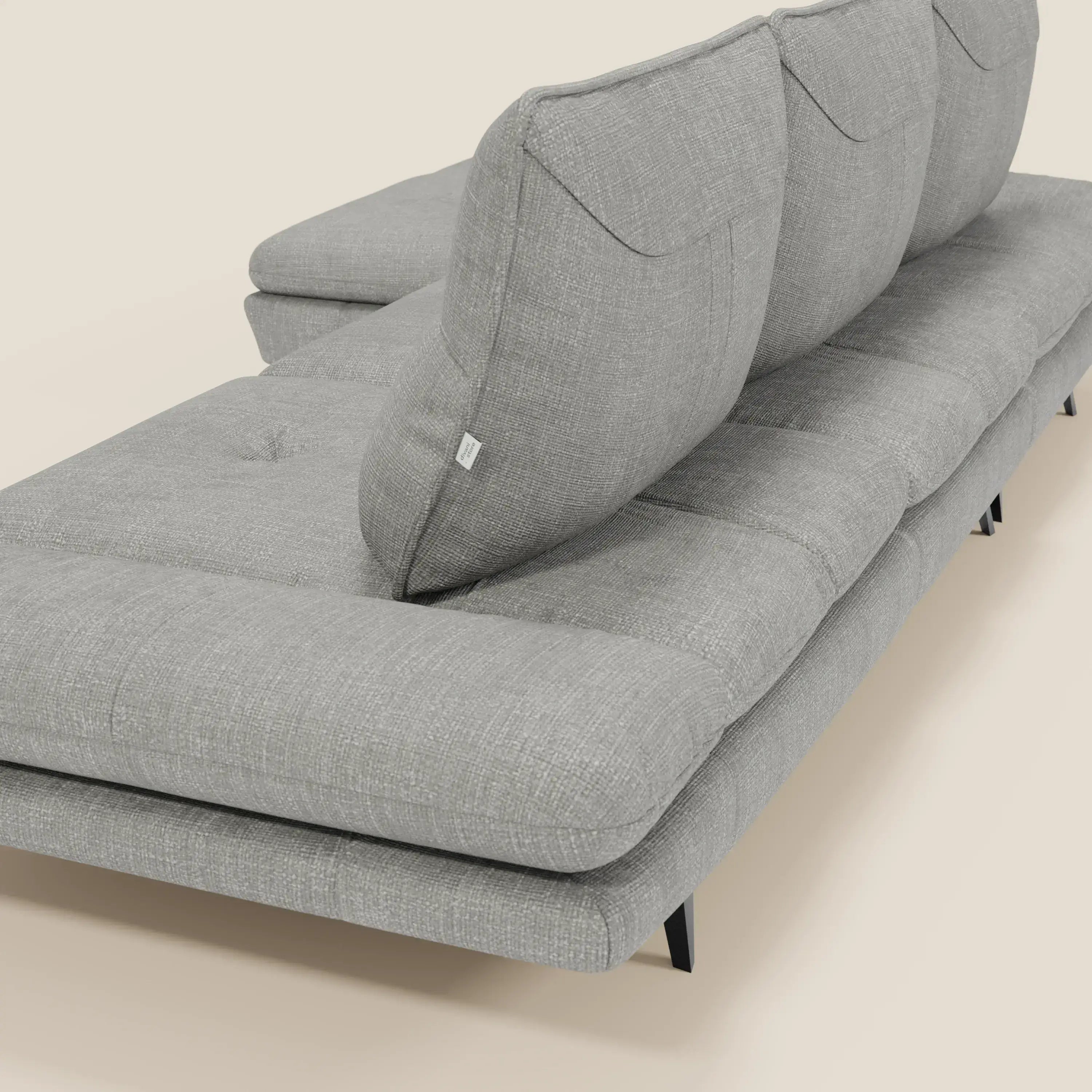 Il Divano con penisola Ardex di Divani.Store, in tessuto impermeabile T06 grigio, è caratterizzato da schienali traslanti, braccioli regolabili e sottili gambe in metallo nero. La texture moderna e le cuciture spiccano su uno sfondo beige chiaro.