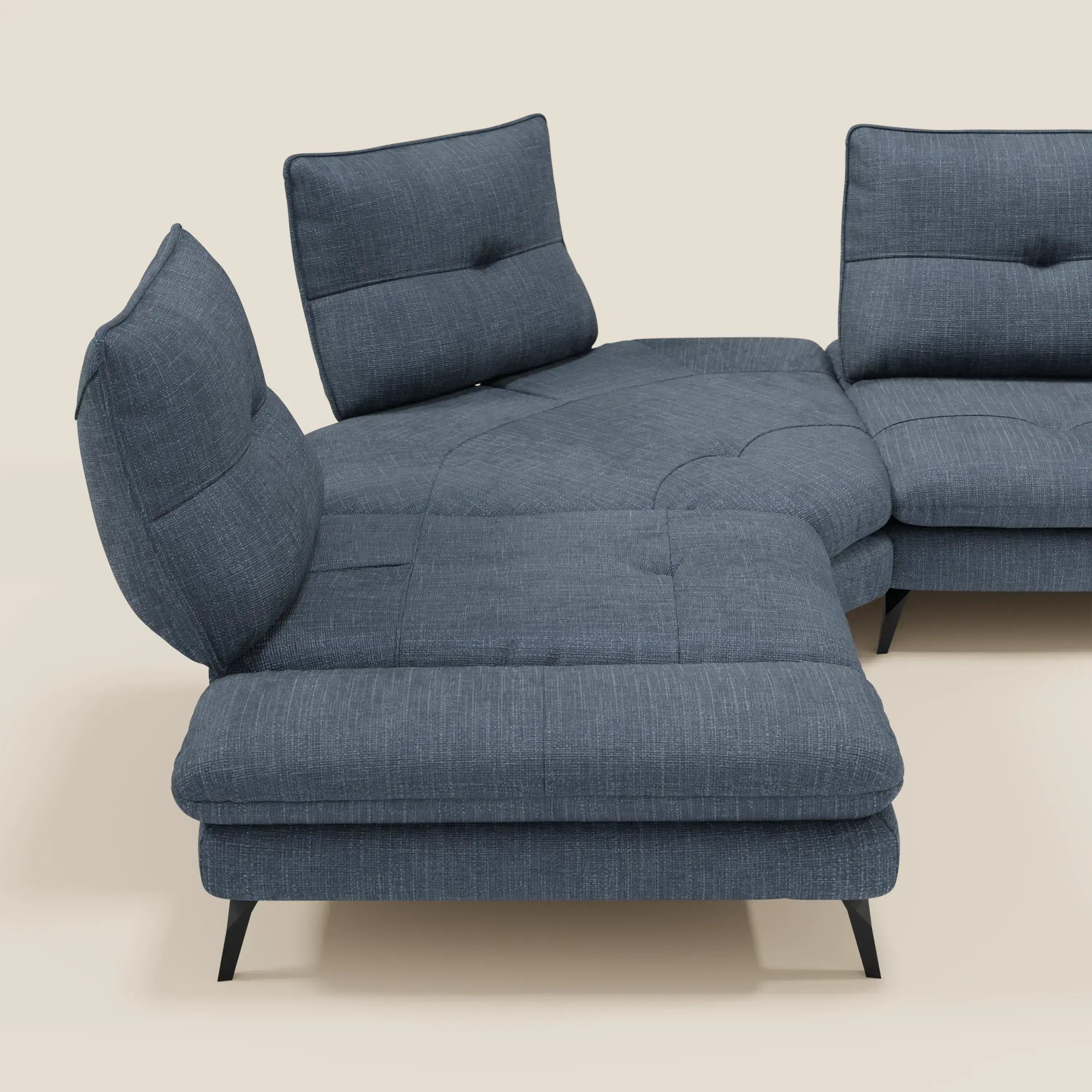 L'Ardex Divano Angolare di Divani.Store, rivestito in elegante tessuto impermeabile blu T06, è caratterizzato da schienali scorrevoli con diverse angolazioni, bracciolo mobile, cuscini trapuntati e gambe in metallo angolate nere su uno sfondo beige chiaro.