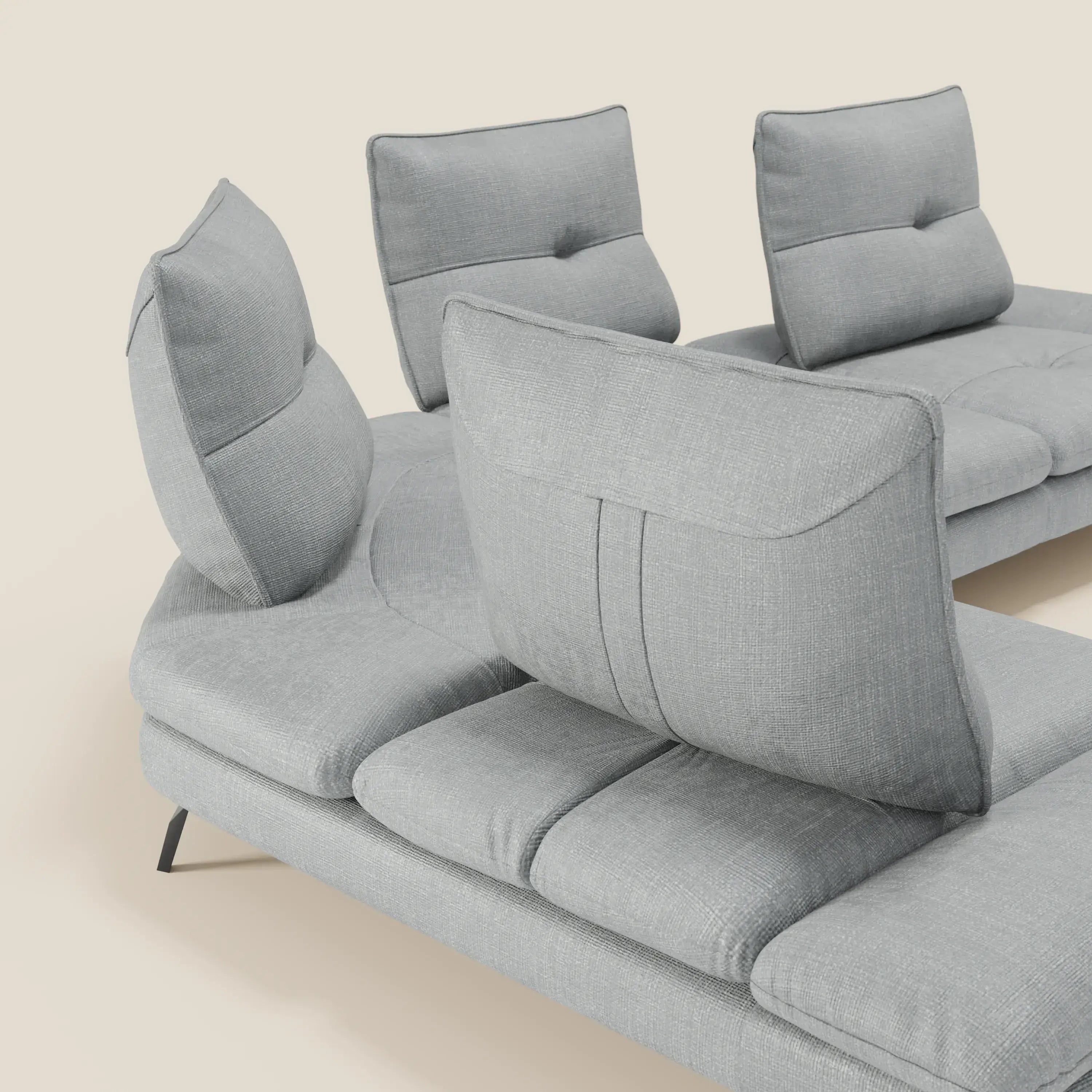 Ardex Divano Angolare di Divani.Store è caratterizzato da schienali traslanti e bracciolo regolabile in elegante tessuto impermeabile T06 ghiaccio, abbinato a sottili gambe nere per un look moderno e sofisticato su uno sfondo bianco sporco.