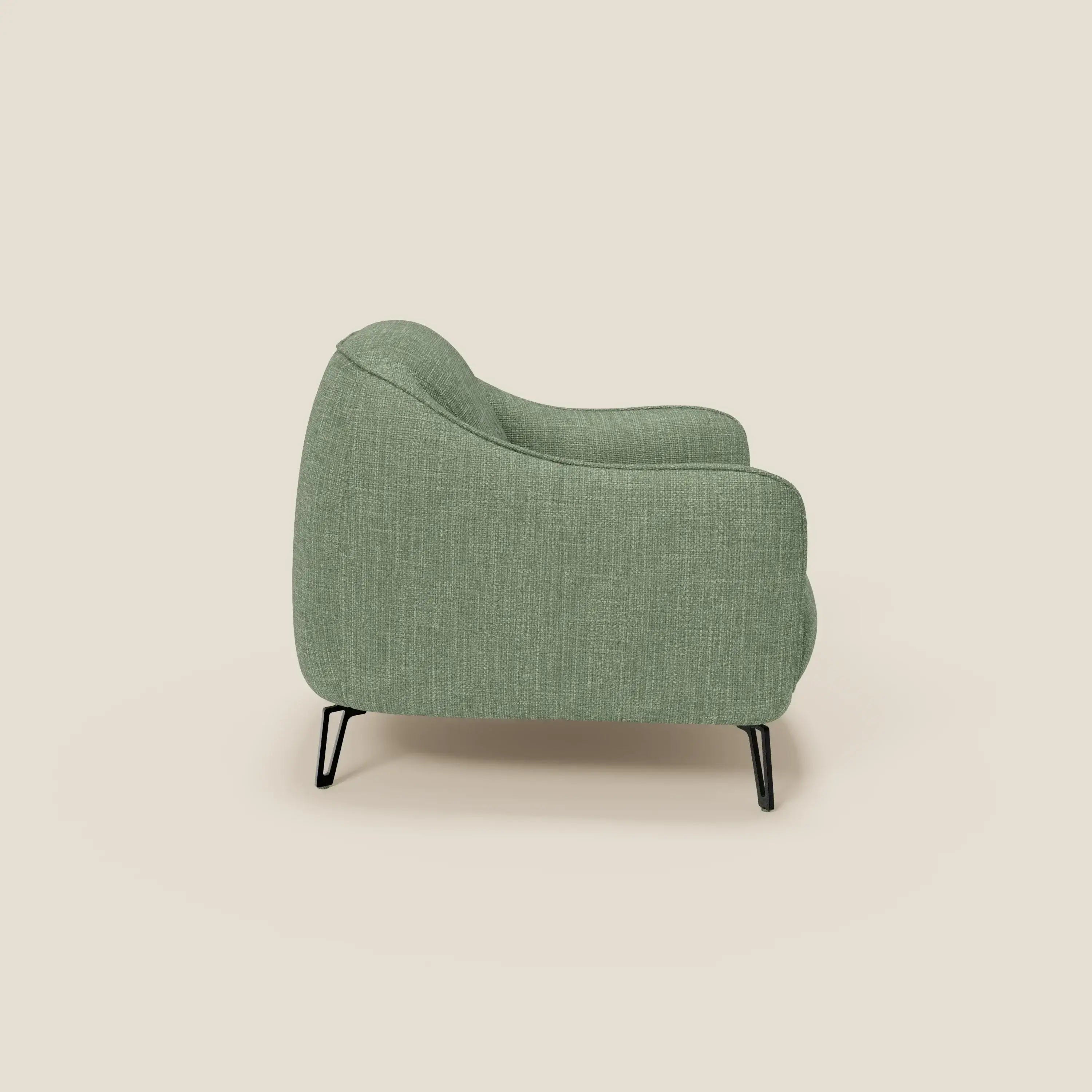 L'Avela Poltroncina di Divani.Store, presentata in tessuto impermeabile T06 verde salvia dalla texture morbida, è caratterizzata da bordi arrotondati e gambe in metallo nero e offre un comfort senza tempo, esposto su uno sfondo beige chiaro.