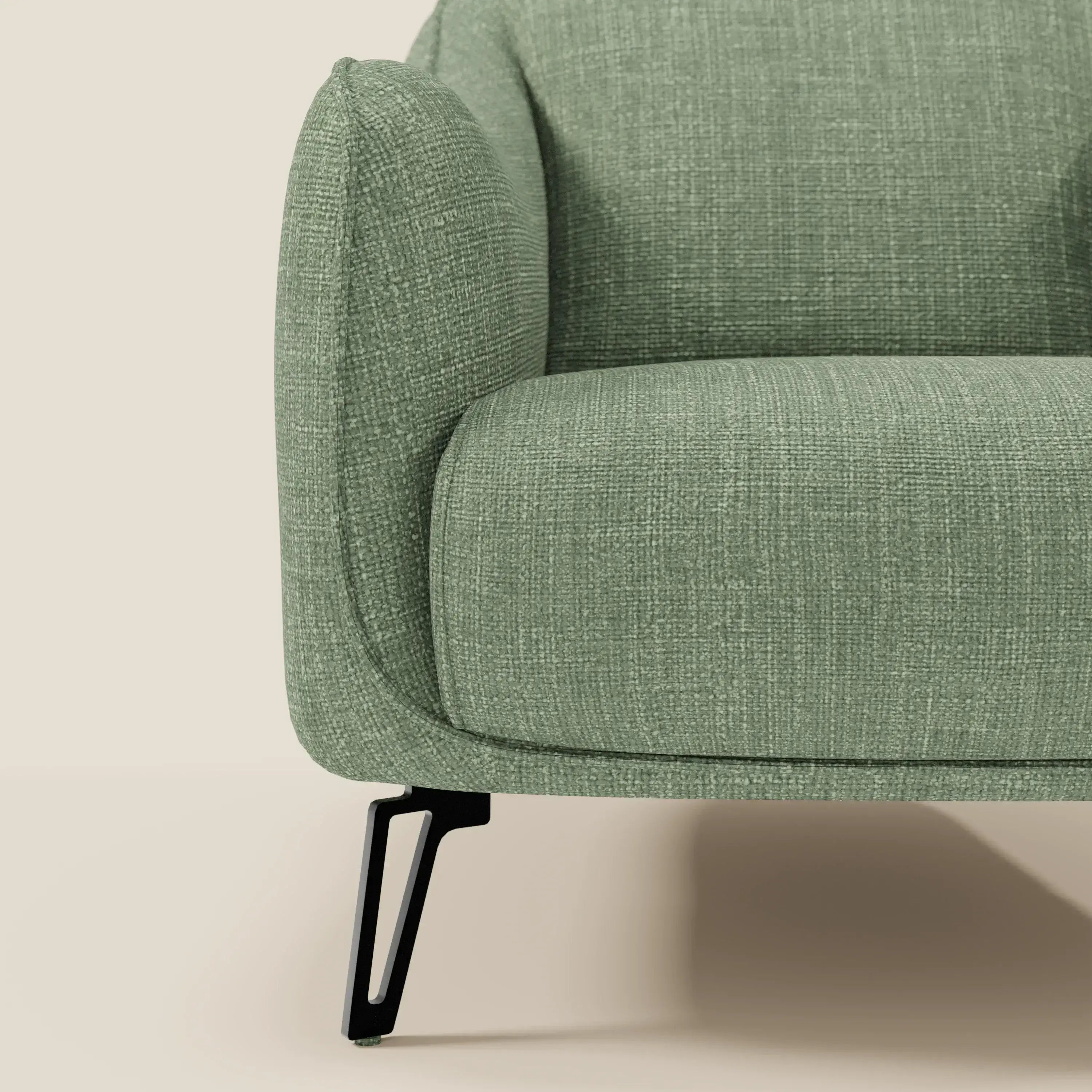 Primo piano di Avela Poltroncina di Divani.Store: un comfort senza tempo in morbido tessuto impermeabile verde salvia T06. L'elegante gamba in metallo nero contrasta con il fondo beige per un tocco di raffinata modernità.