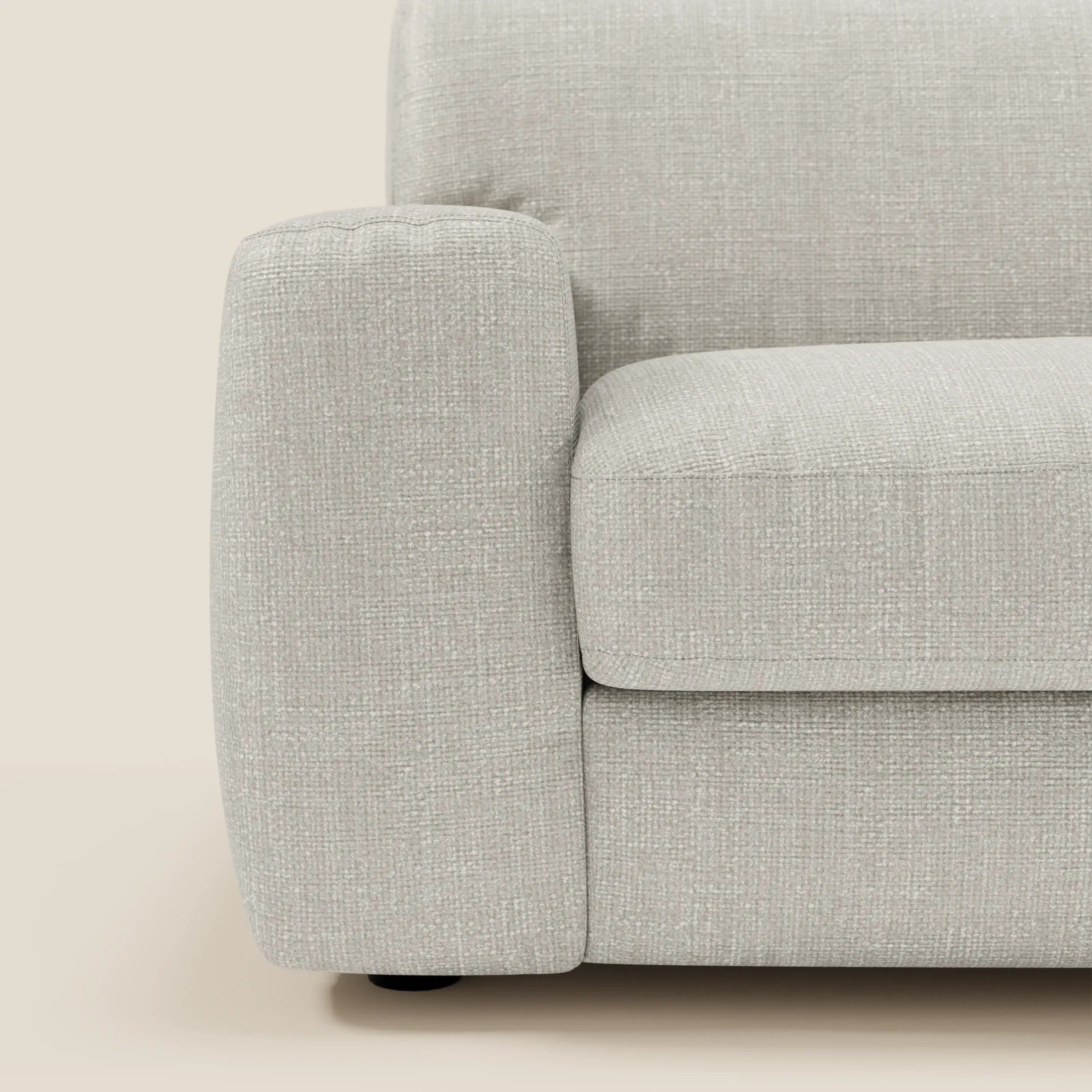 Primo piano di Cloud Divano letto materasso H17 cm di Divani.Store che mostra il bracciolo sinistro in tessuto impermeabile T06 grigio chiaro. Tra le caratteristiche, i morbidi cuscini, le linee pulite e i piedini neri rotondi su uno sfondo beige neutro.