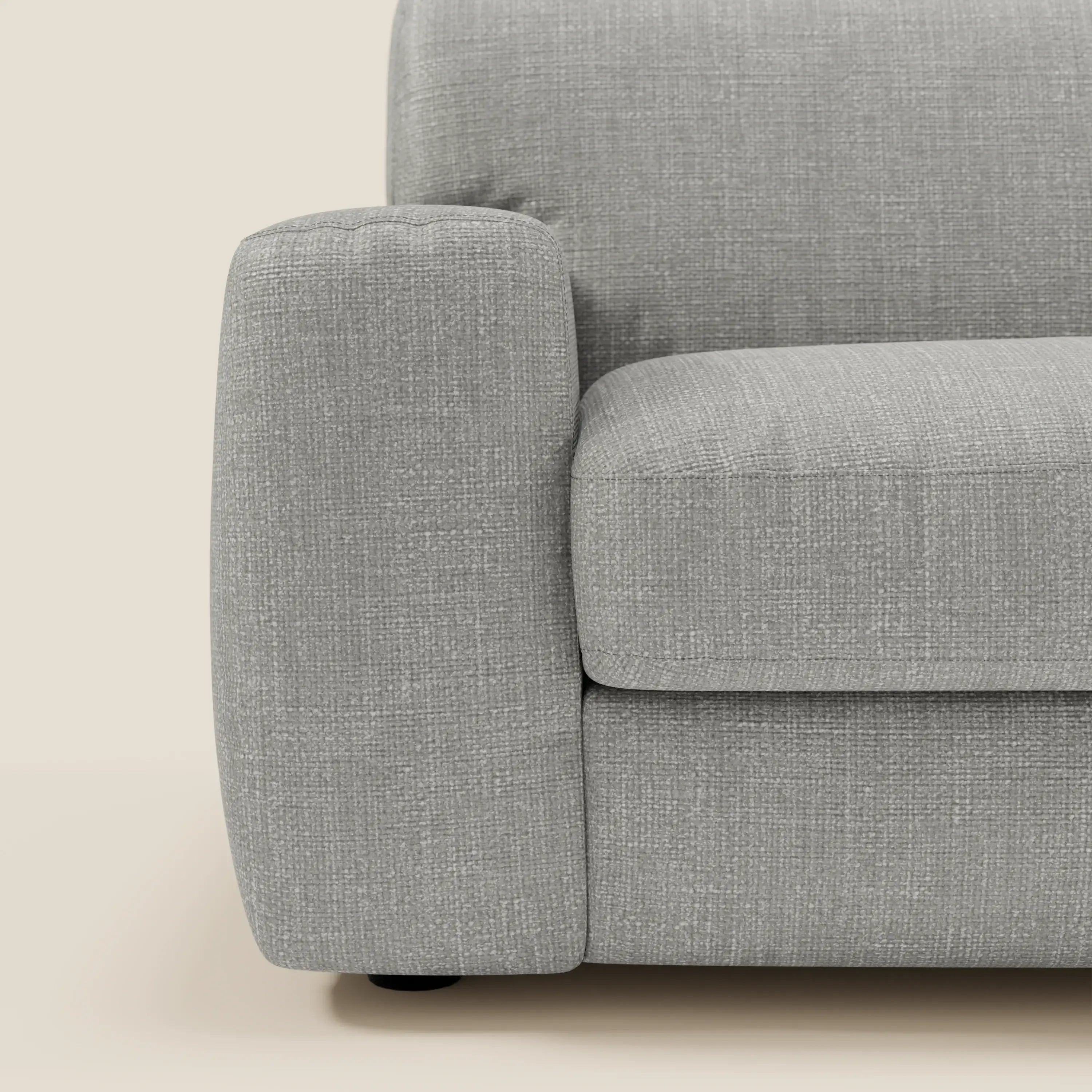 Un primo piano di Cloud Divano letto materasso H17 cm di Divani.Store mostra il suo bracciolo quadrato e spesso e i cuscini impermeabili grigio T06. Su uno sfondo beige, è visibile solo la metà sinistra di questo divano letto moderno.