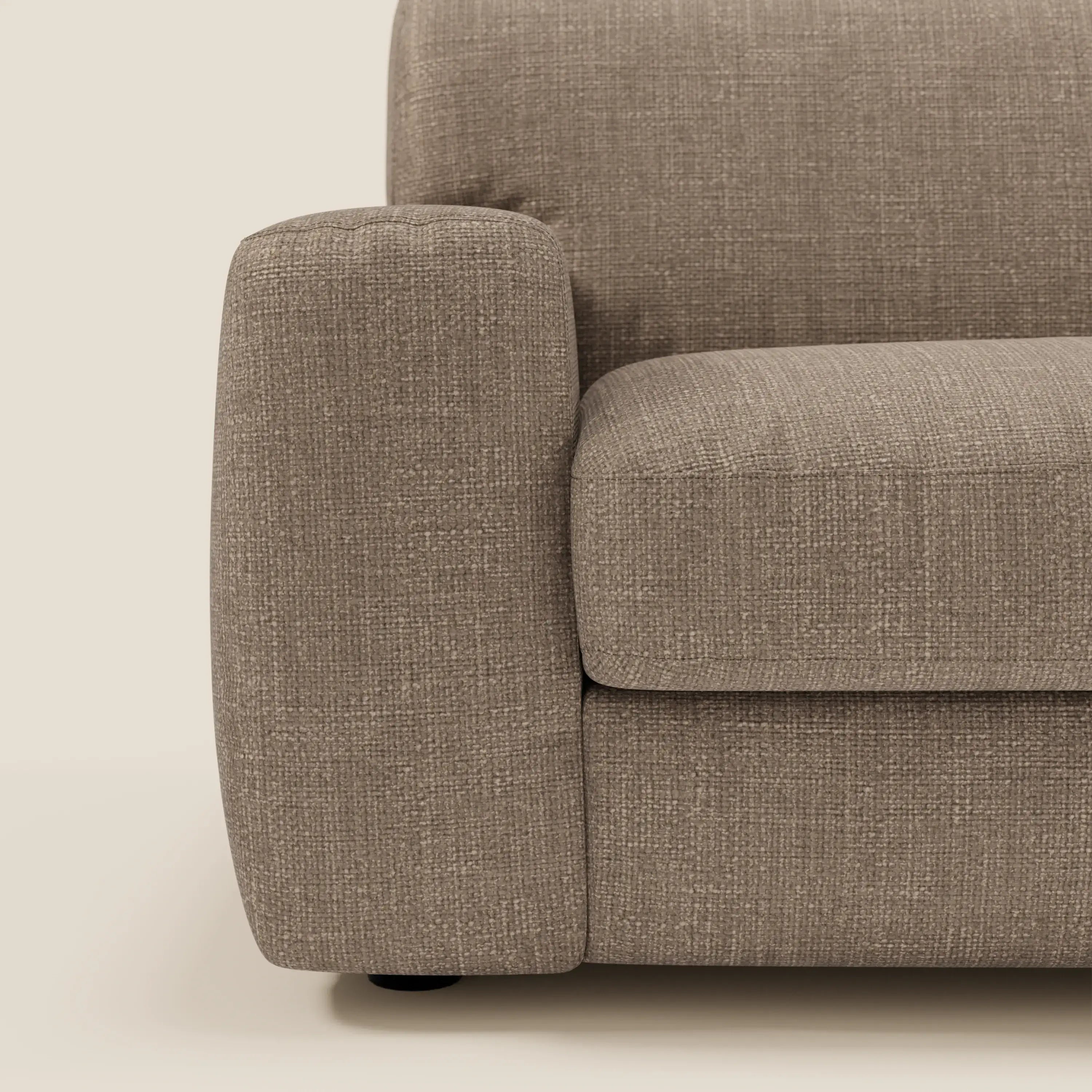 Un primo piano del braccio sinistro e della seduta di Cloud Divano letto materasso H17 cm di Divani.Store mostra il suo tessuto marrone T06 testurizzato e impermeabile, con linee squadrate e cuscini morbidi che si fondono con il fondo beige chiaro.