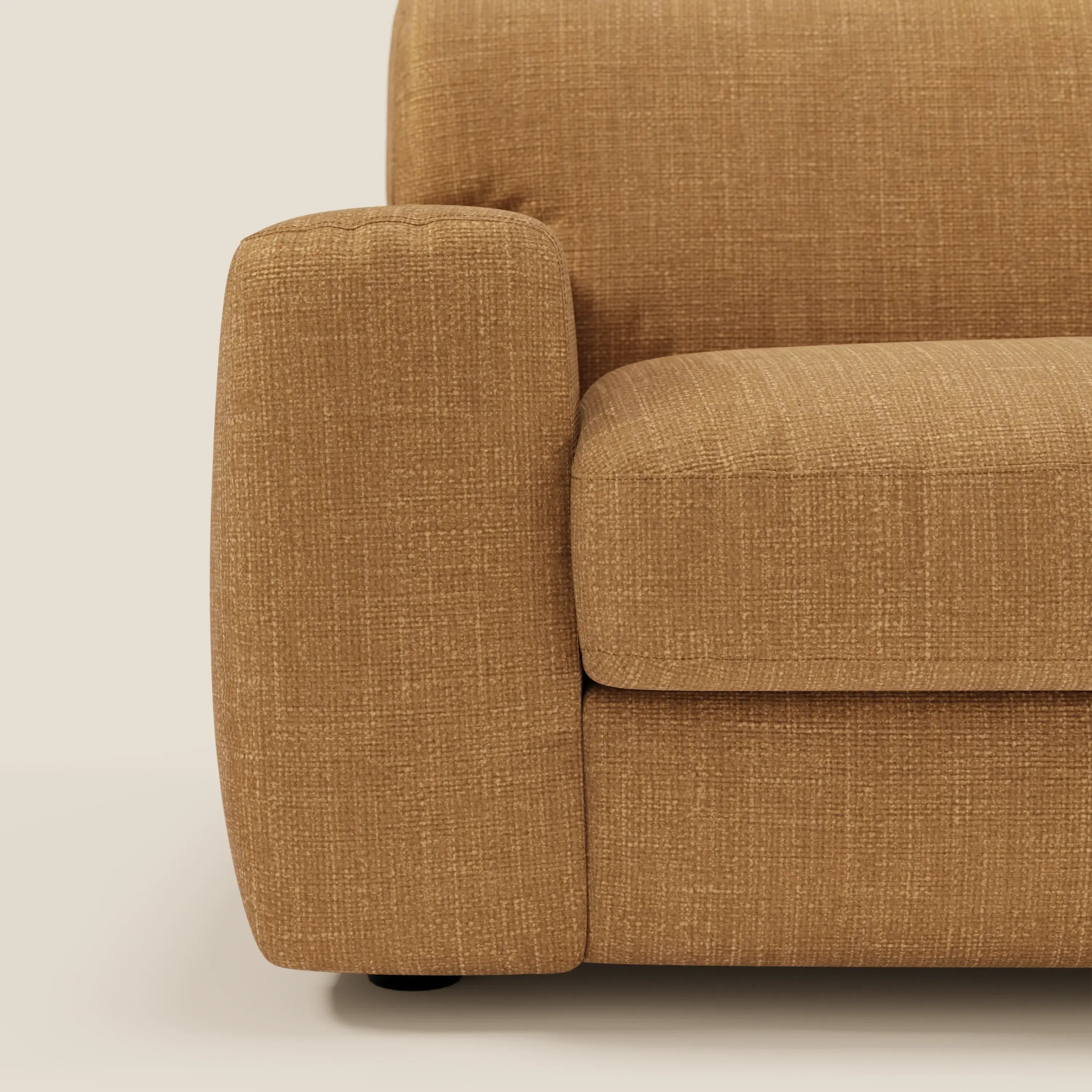 Primo piano del bracciolo sinistro e del cuscino di seduta di Cloud Divano letto materasso H17 cm di Divani.Store, in tessuto impermeabile ocra T06. Il fondo bianco sporco mette in risalto i morbidi cuscini e la texture contemporanea.
