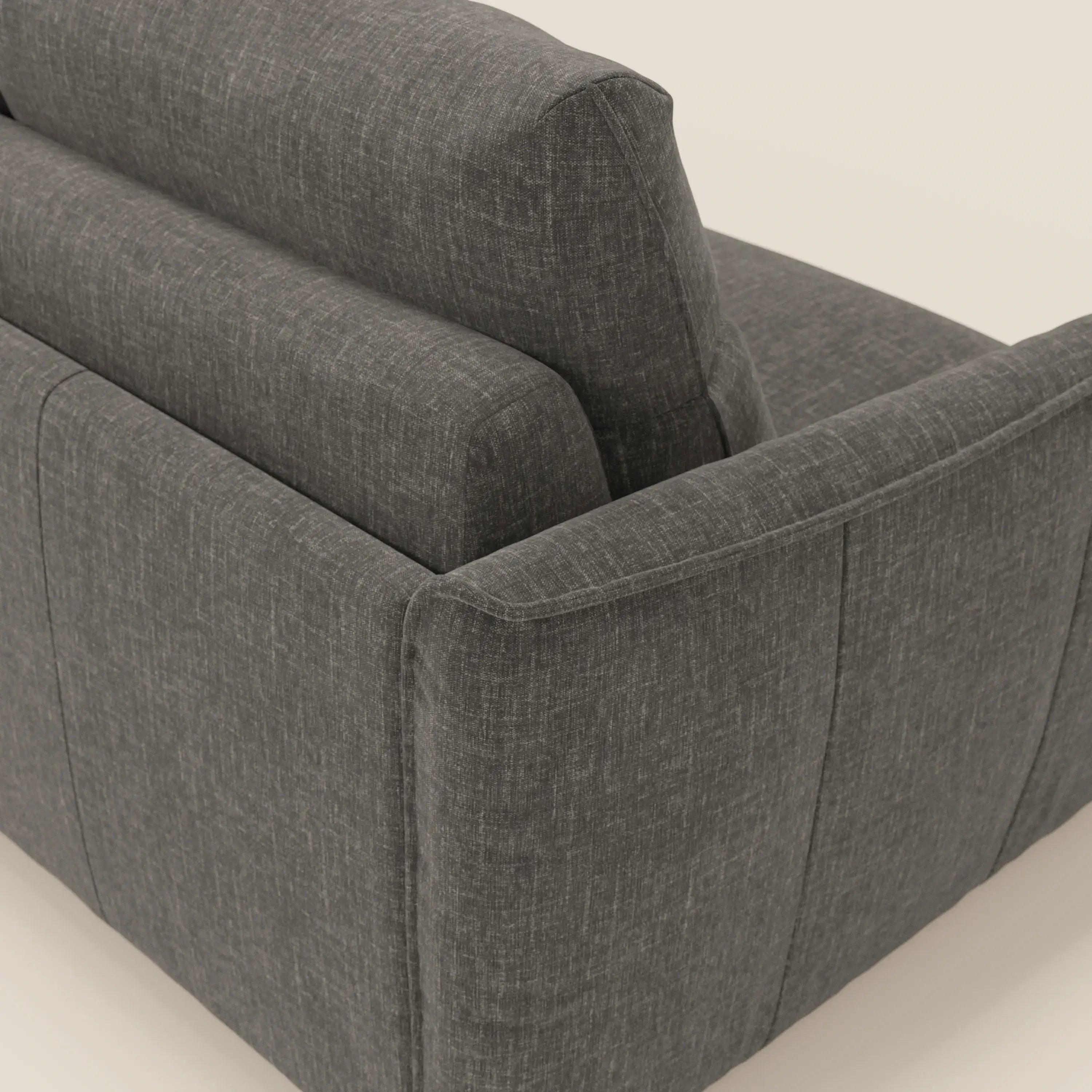 Un primo piano di Elios Divano letto di Divani.Store mostra gli spessi cuscini dello schienale e il bracciolo in tessuto smacchiabile T24 antracite con cuciture a vista, che spiccano su uno sfondo bianco sporco.