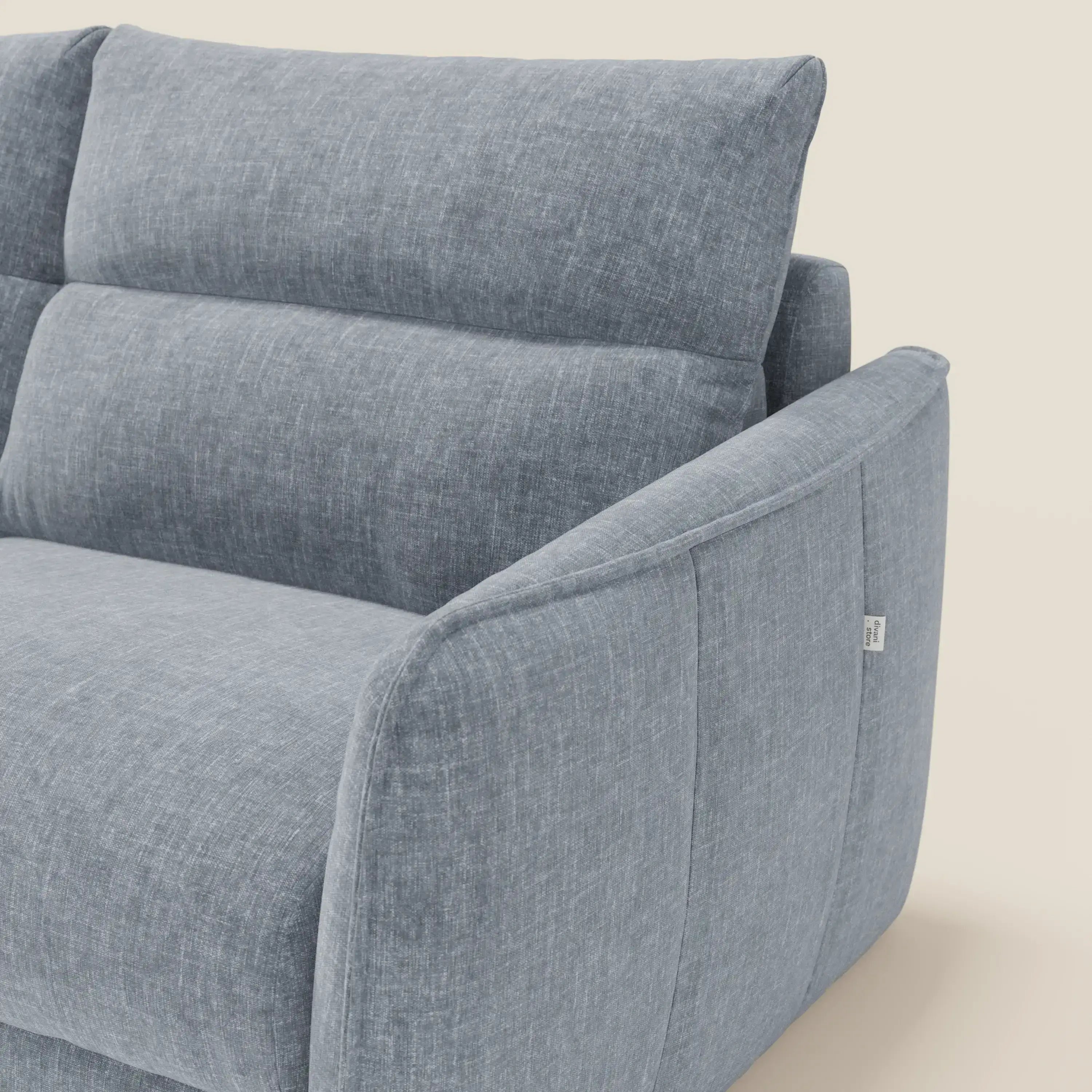 Un primo piano di Elios Divano letto con morbidi cuscini spalliera in tessuto smacchiabile T24 carta da zucchero di Divani.Store mostra i cuscini morbidi e il bracciolo angolato, con un'etichetta in tessuto bianco sulla cucitura laterale su uno sfondo chiaro.