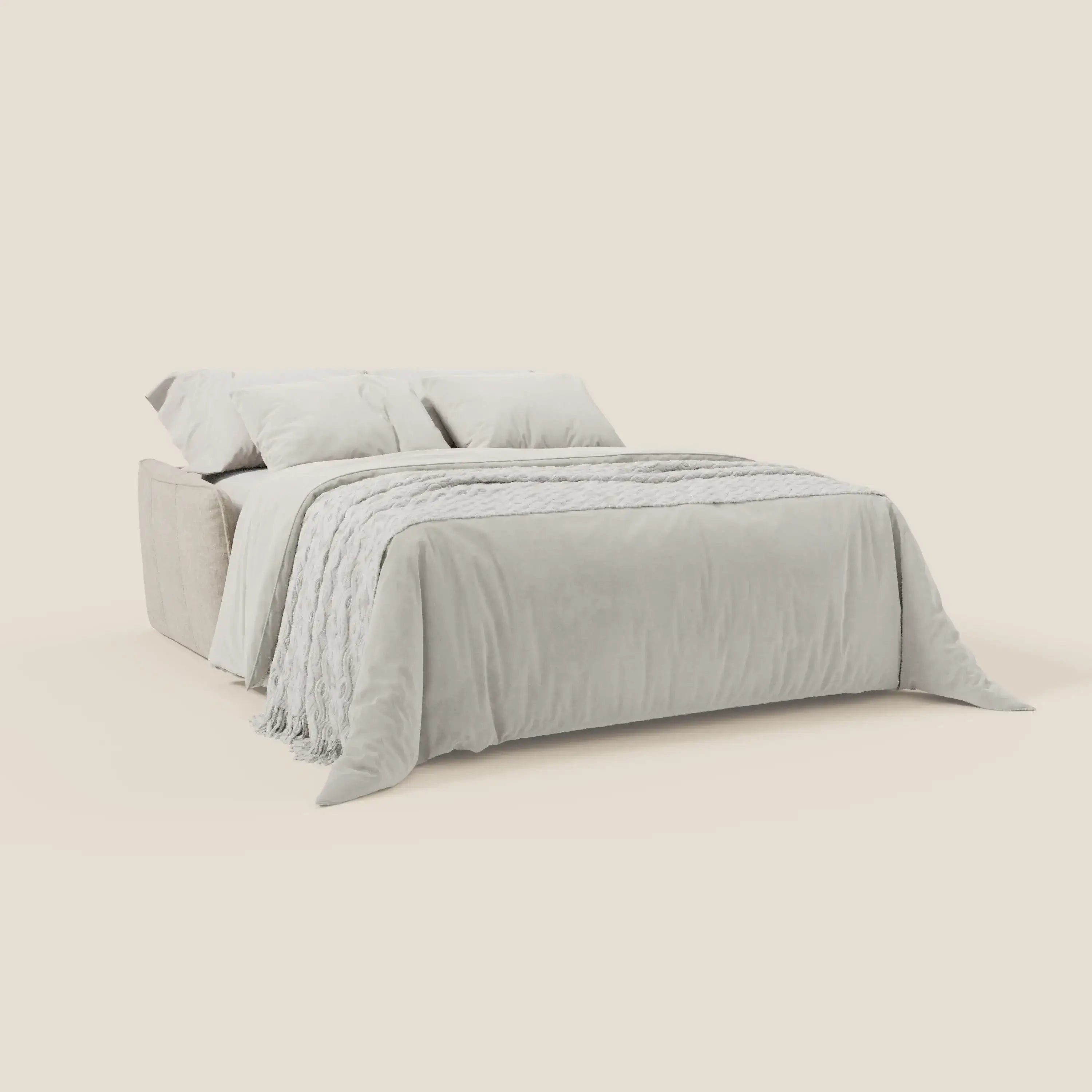 Il divano letto Elios di Divani.Store è caratterizzato da morbidi cuscini di schienale in tessuto antimacchia T24 bianco latte. Abbinato a una biancheria da letto grigio chiaro e a un copriletto strutturato, si staglia su uno sfondo beige chiaro per un look moderno.