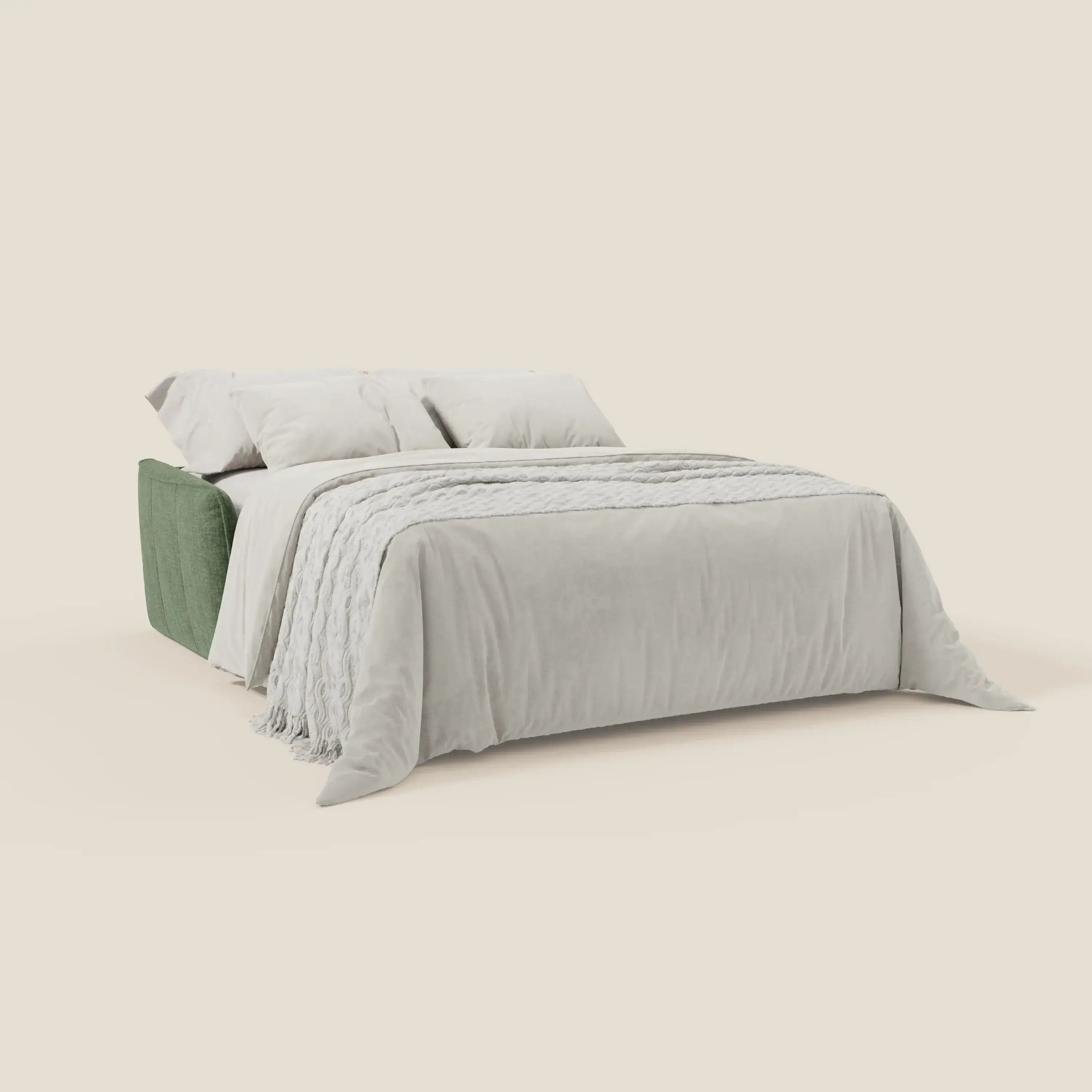 Il Divano letto Elios di Divani.Store, con morbidi cuscini in tessuto antimacchia T24 verde oliva, è presentato con un piumone grigio chiaro, una coperta testurizzata e due cuscini grigio chiaro su uno sfondo beige semplice.