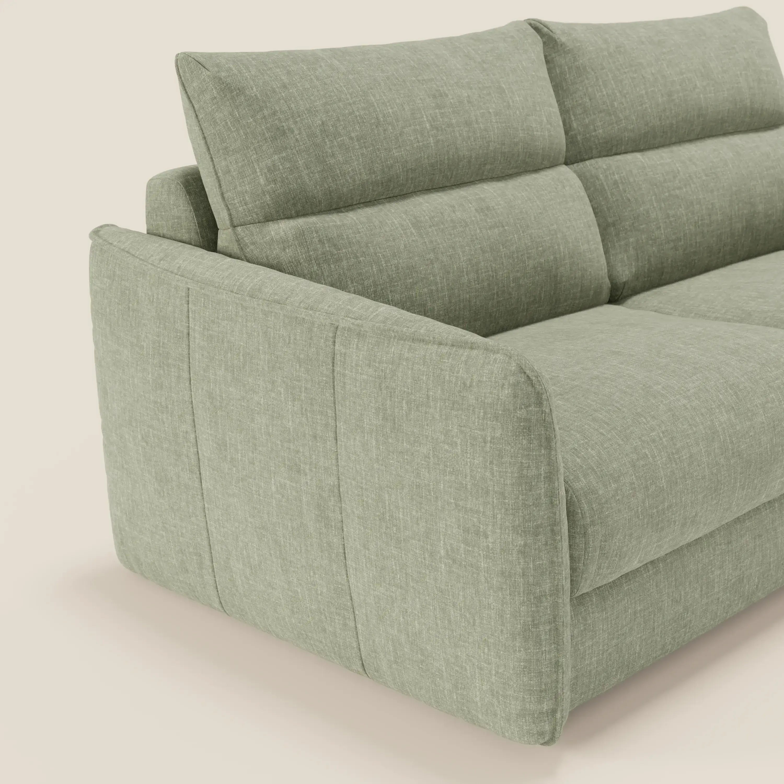 Una vista angolata e ravvicinata di Elios Divano letto con morbidi cuscini spalliera in tessuto smacchiabile T24 verde salvia di Divani.Store, caratterizzato da cuscini morbidi, ampi braccioli e una finitura strutturata su un morbido sfondo bianco sporco.