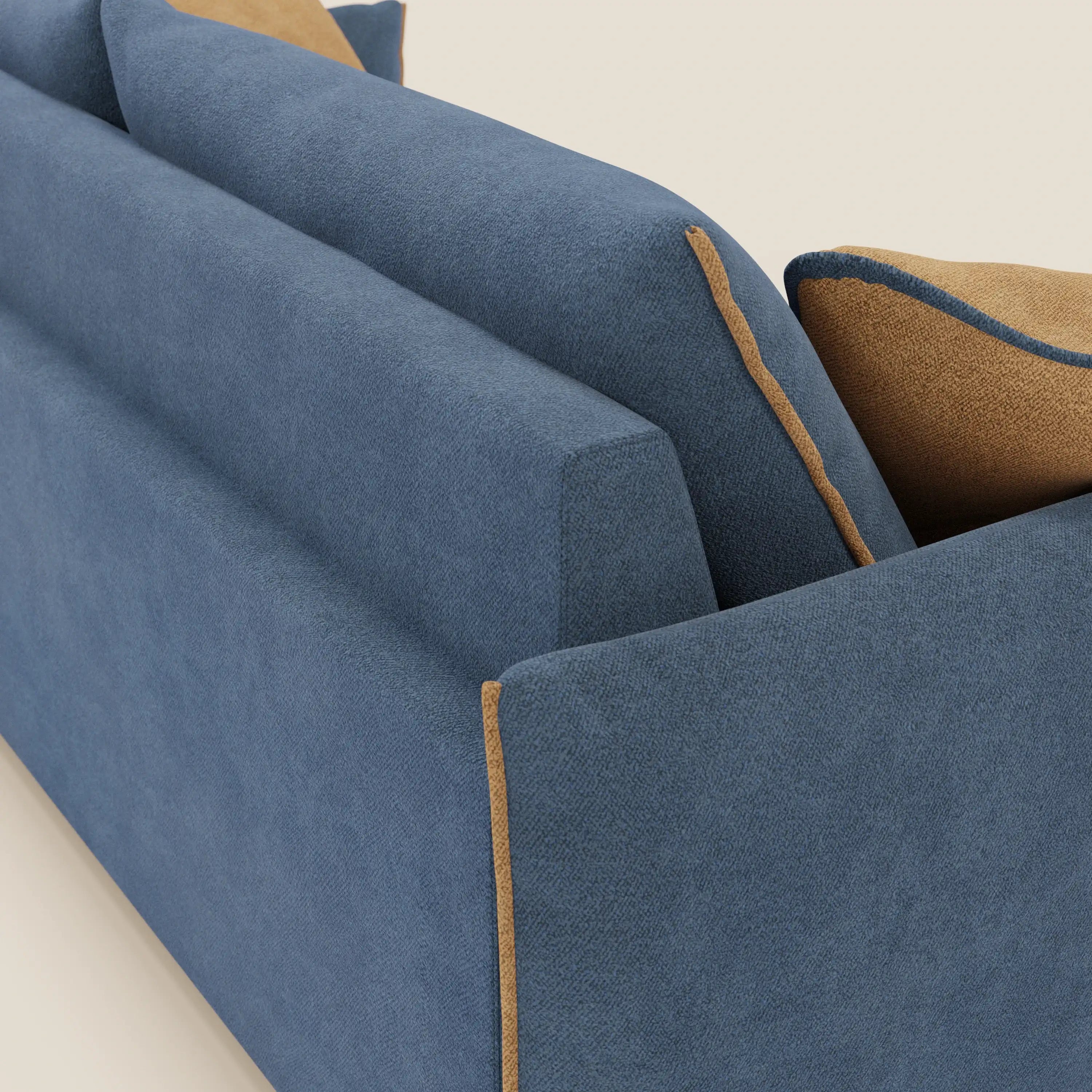 Un primo piano del divano Flexar di Divani.Store in morbido bouclé impermeabile T07 blu-arancio mostra lo schienale e il bracciolo con profili a contrasto. Due cuscini, blu con profili arancioni e arancione con blu, poggiano sul divano su uno sfondo beige chiaro.