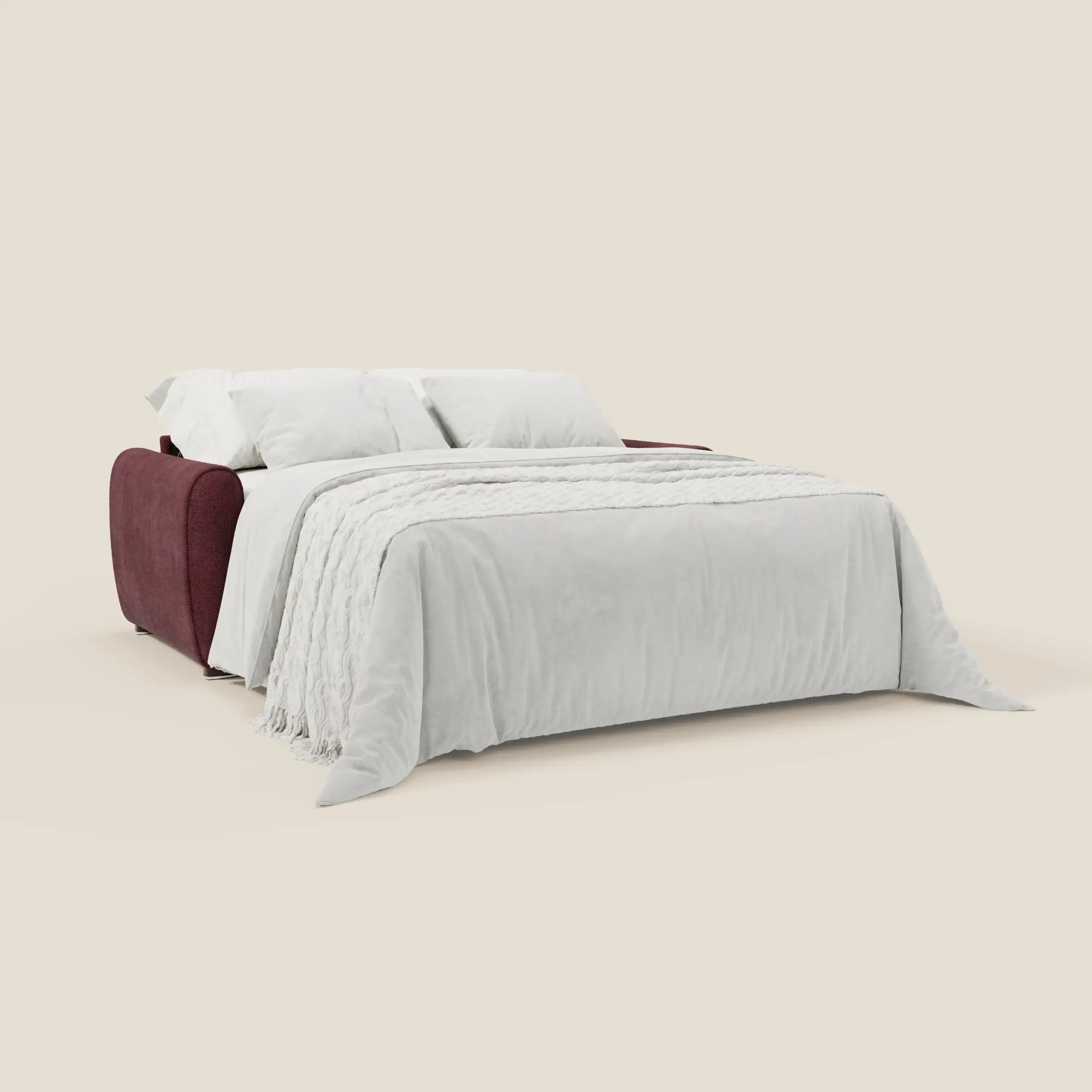 Il divano letto Kaleo moderno di Divani.Store, in tessuto impermeabile T26 bordeaux prugna con materasso H17 cm, è aperto a letto e sfoggia un look contemporaneo con copriletto bianco e due grandi cuscini bianchi.