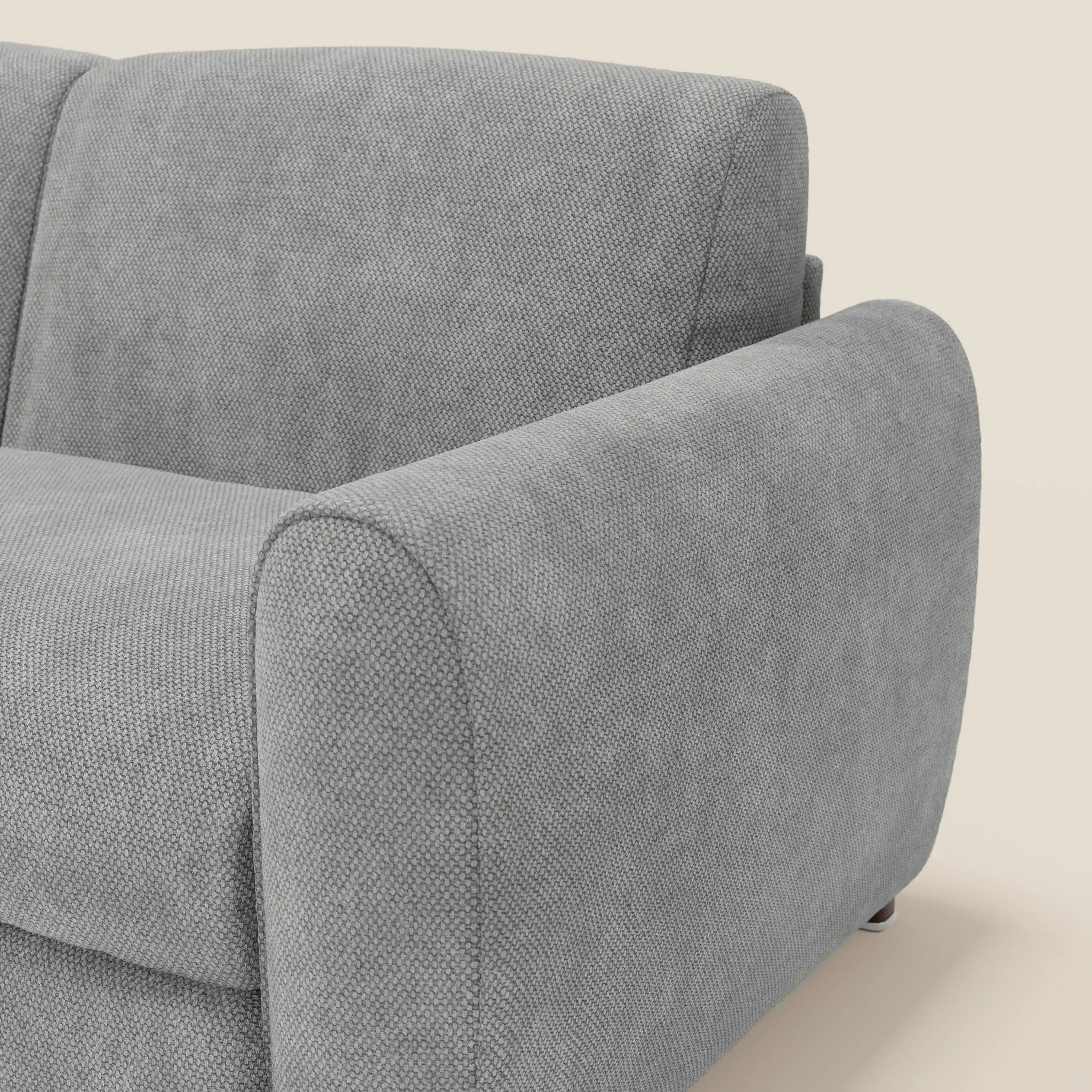 Primo piano del divano letto moderno Kaleo con materasso H17 cm di Divani.Store, in raffinato tessuto impermeabile T26 grigio, con schienale in feltro e ampi braccioli. Il suo design contemporaneo spicca su uno sfondo beige.