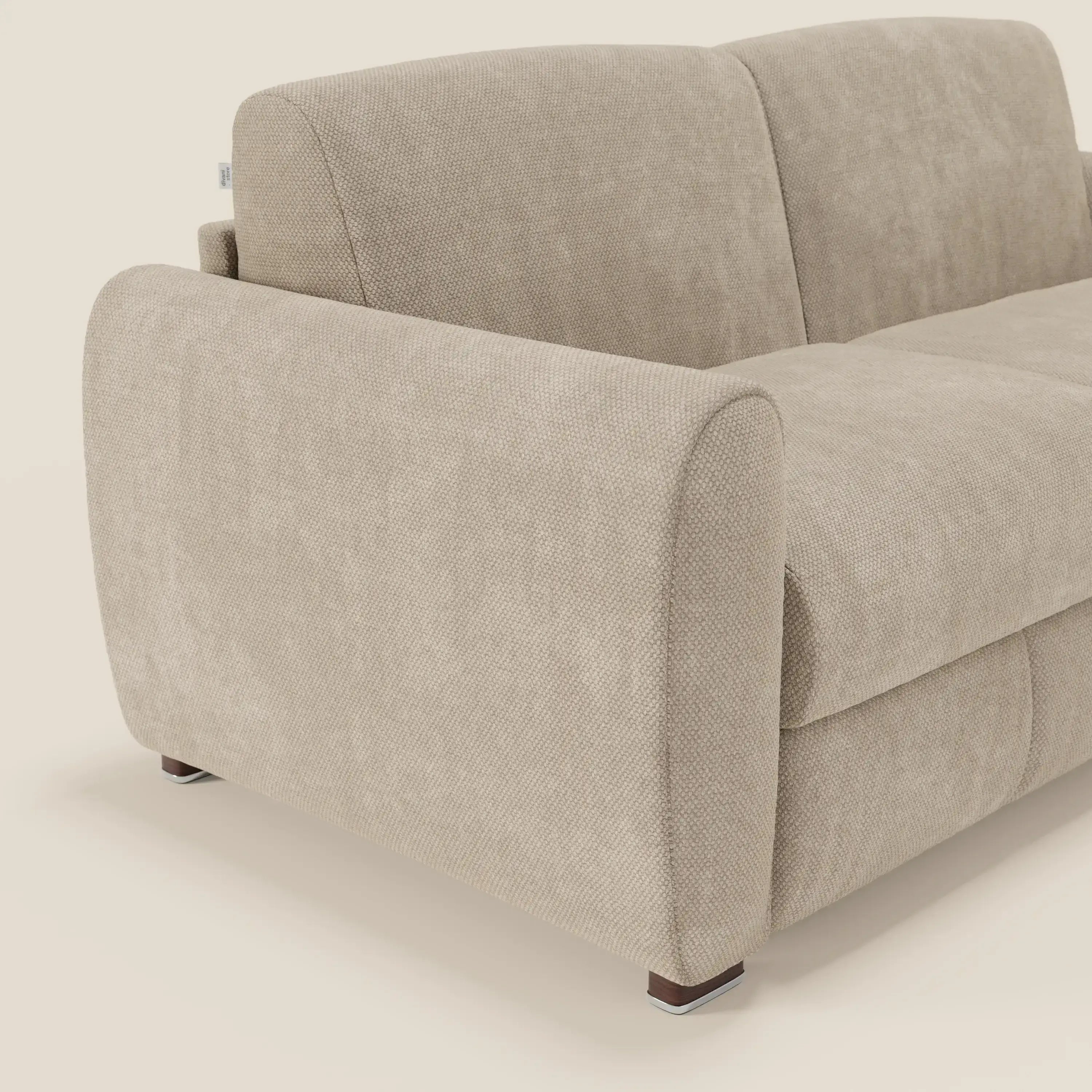 Un primo piano di Kaleo Divano letto moderno di Divani.Store è caratterizzato da cuscini in tessuto, ampi braccioli curvi e gambe in legno scuro. Il morbido rivestimento in tessuto impermeabile T26 panna mette in risalto il suo design contemporaneo su uno sfondo semplice.