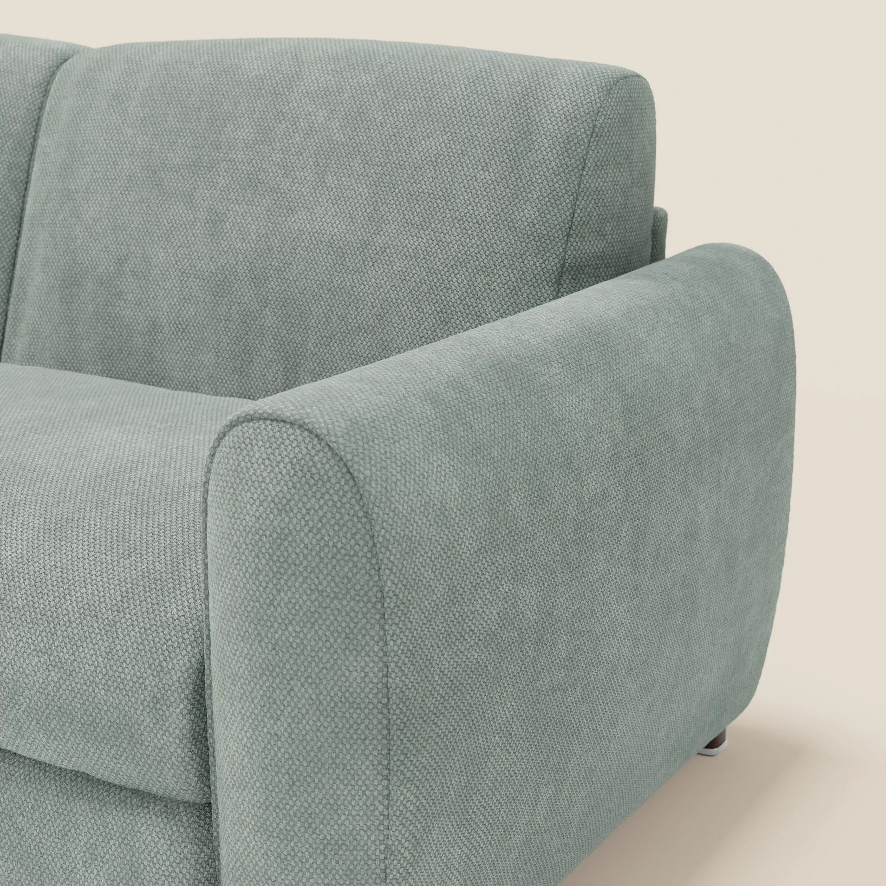 Primo piano del divano letto moderno Kaleo di Divani.Store in raffinato tessuto impermeabile T26 verde acqua, che evidenzia il bracciolo sinistro arrotondato, il cuscino di seduta e lo schienale su uno sfondo bianco sporco.